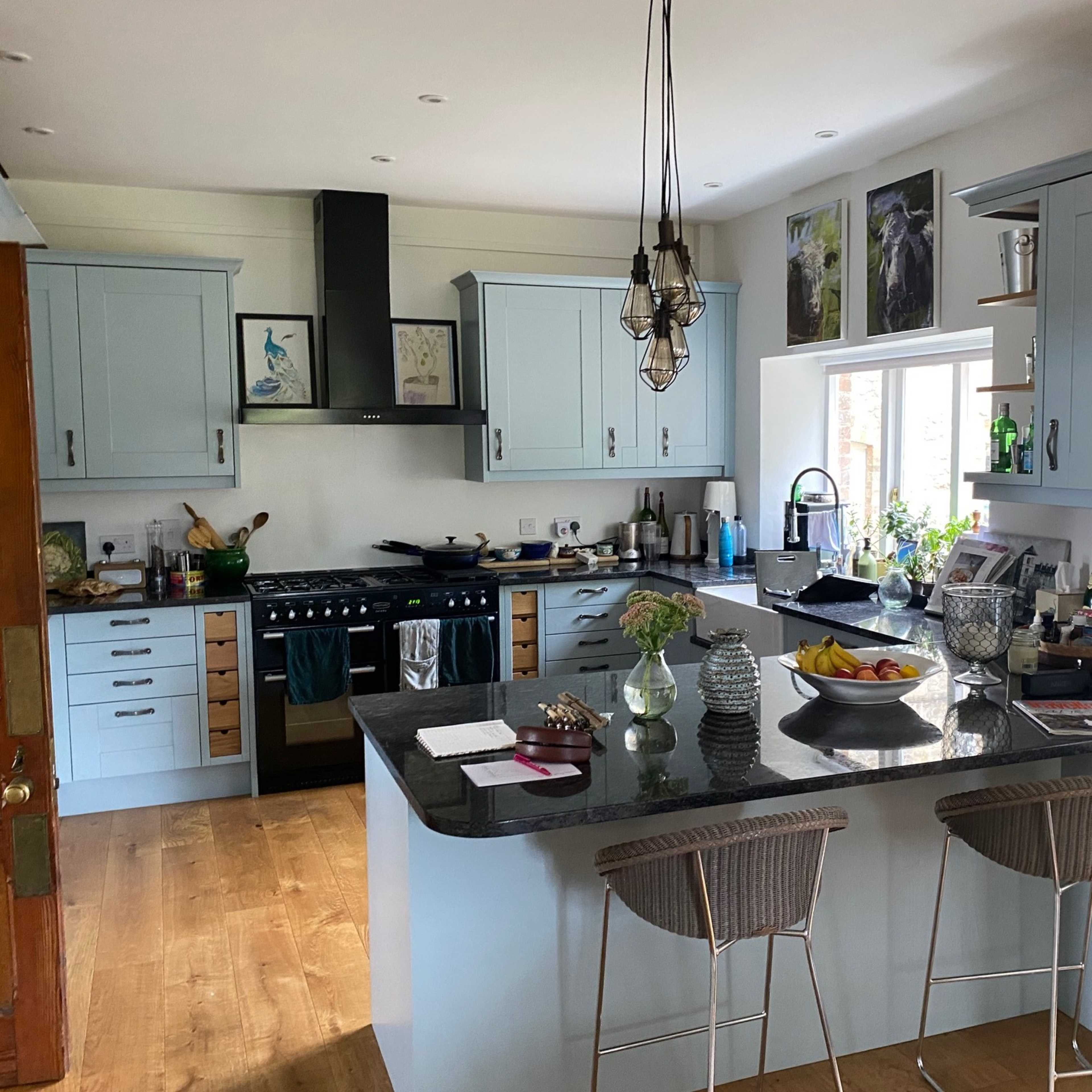 A modern kitchen featuring light blue cabinetry, a dark countertop, and an island with bar stools, alongside various kitchen appliances and decorative items.