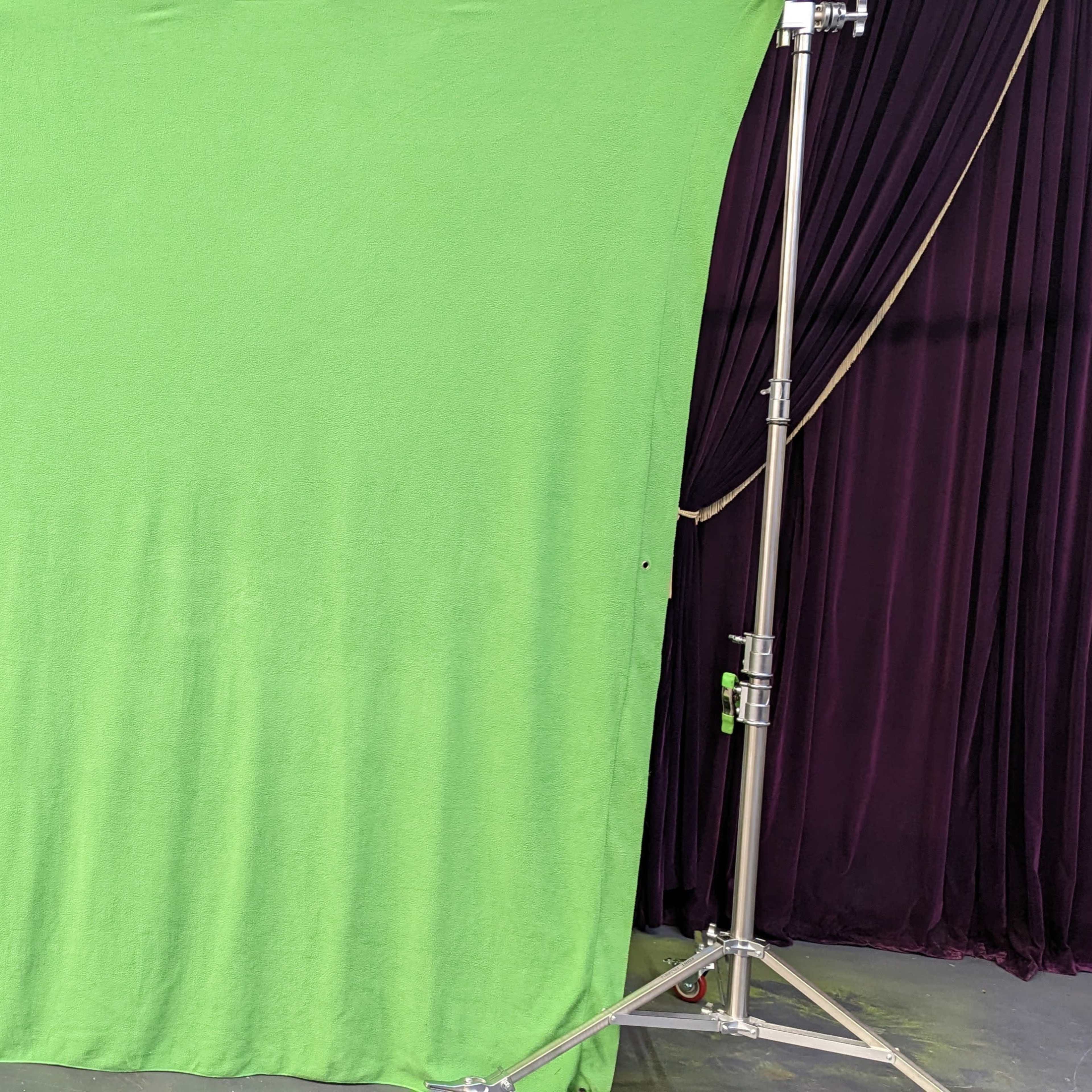 A green screen setup on a metal frame in front of a dark curtain backdrop.