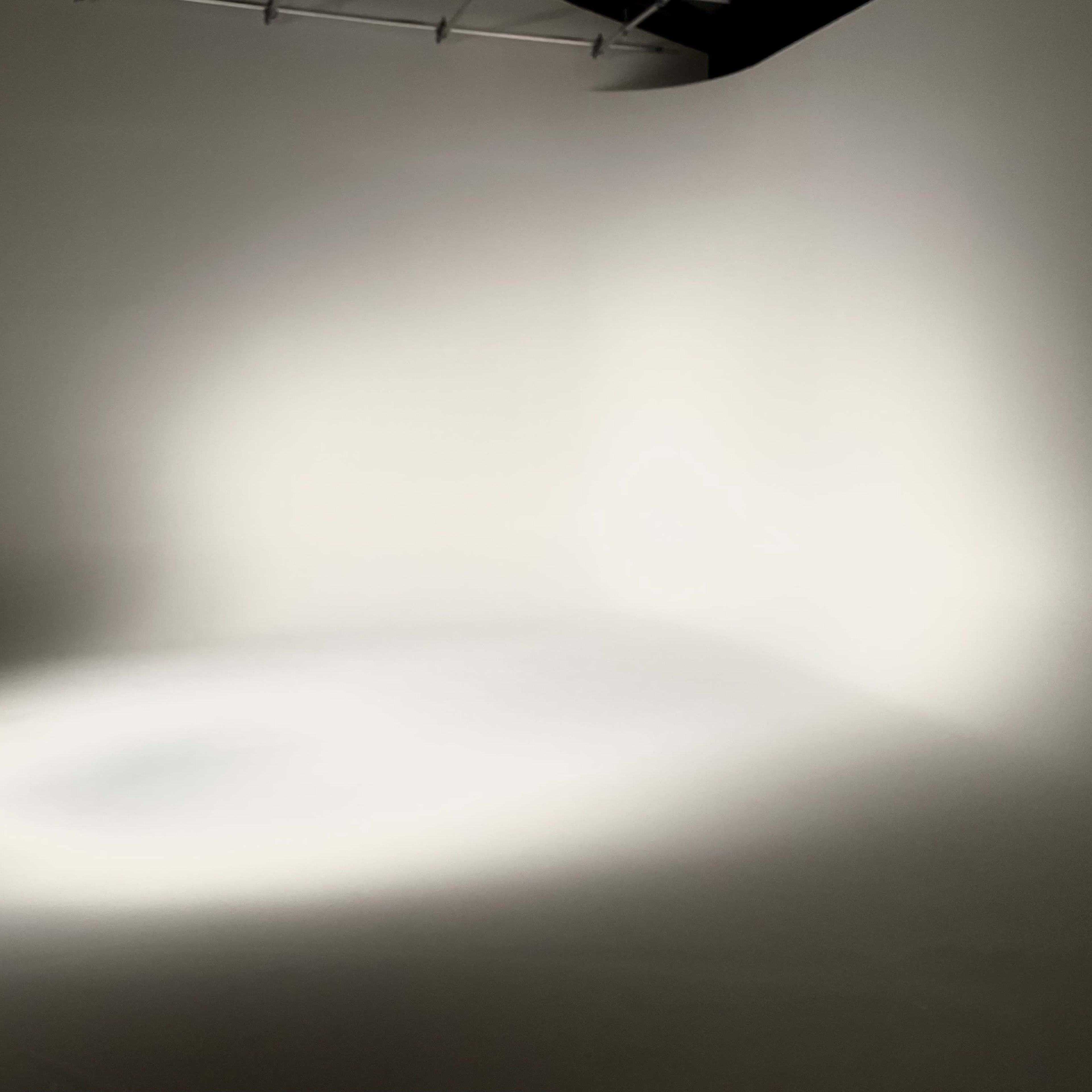 A softly lit studio space with a plain, light-colored background and a subtle light gradient on the floor.