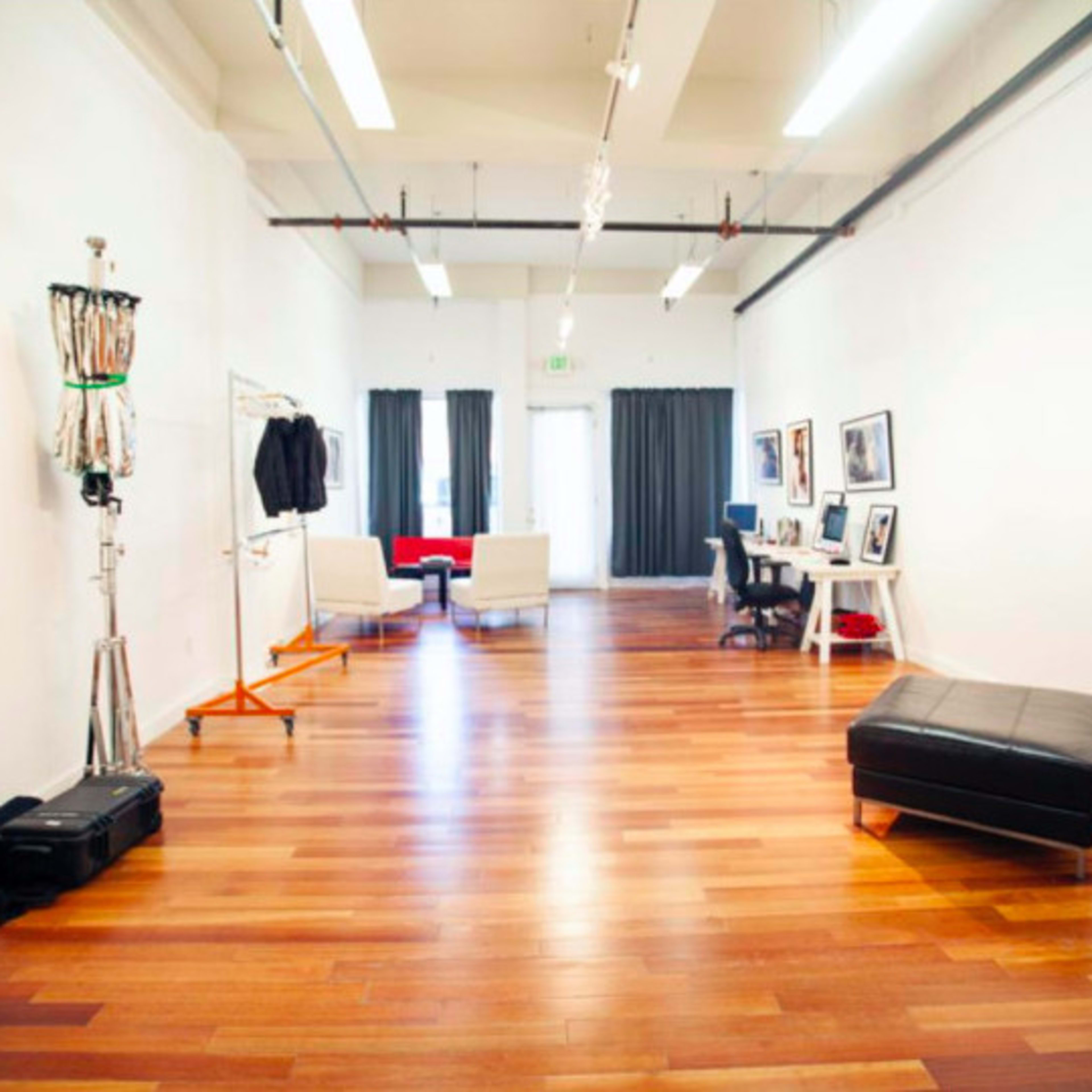 A spacious, well-lit room with wooden flooring, featuring a seating area, a desk setup, and a clothing rack.