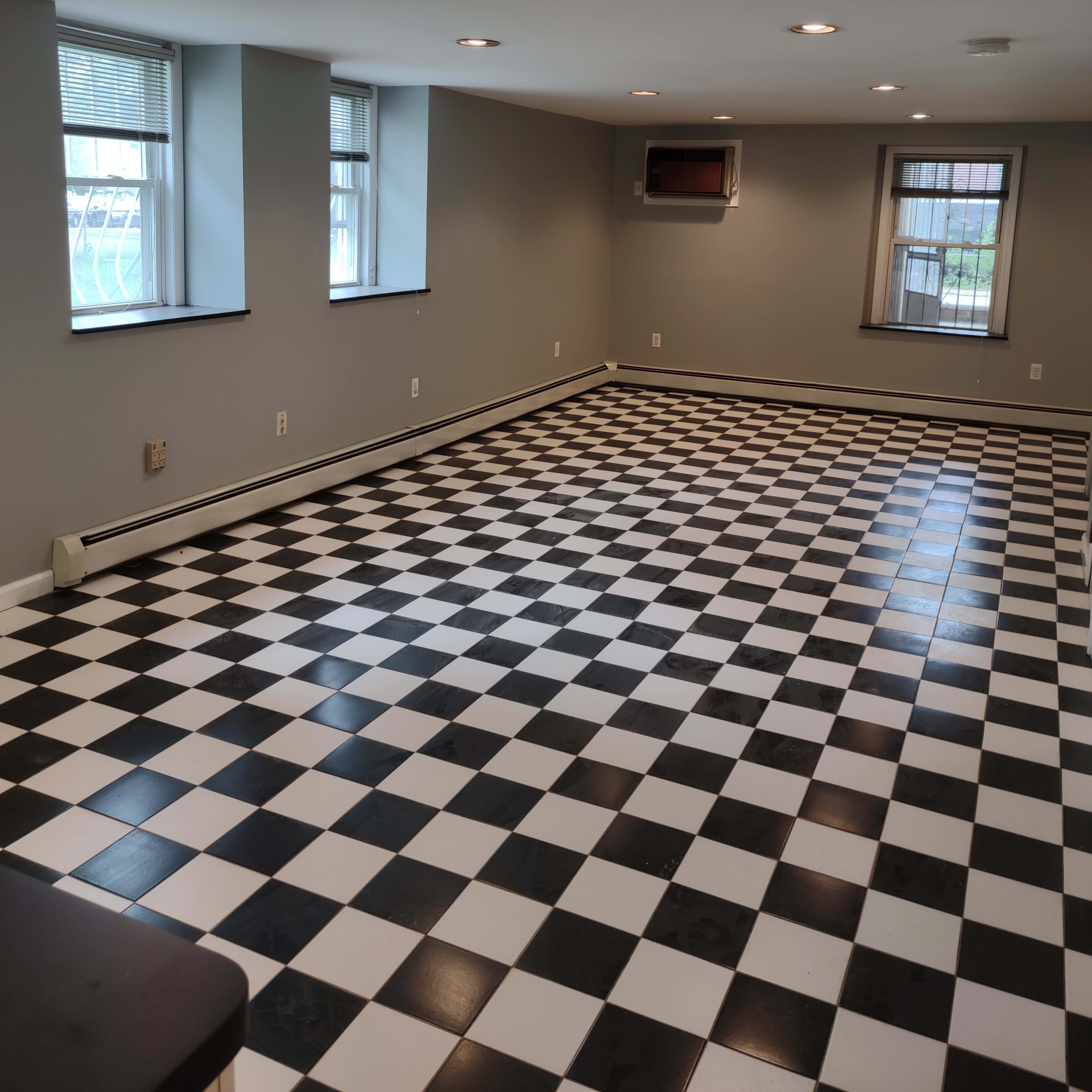 A spacious room with black and white checkered tiles, two windows, and a wall-mounted air conditioning unit.
