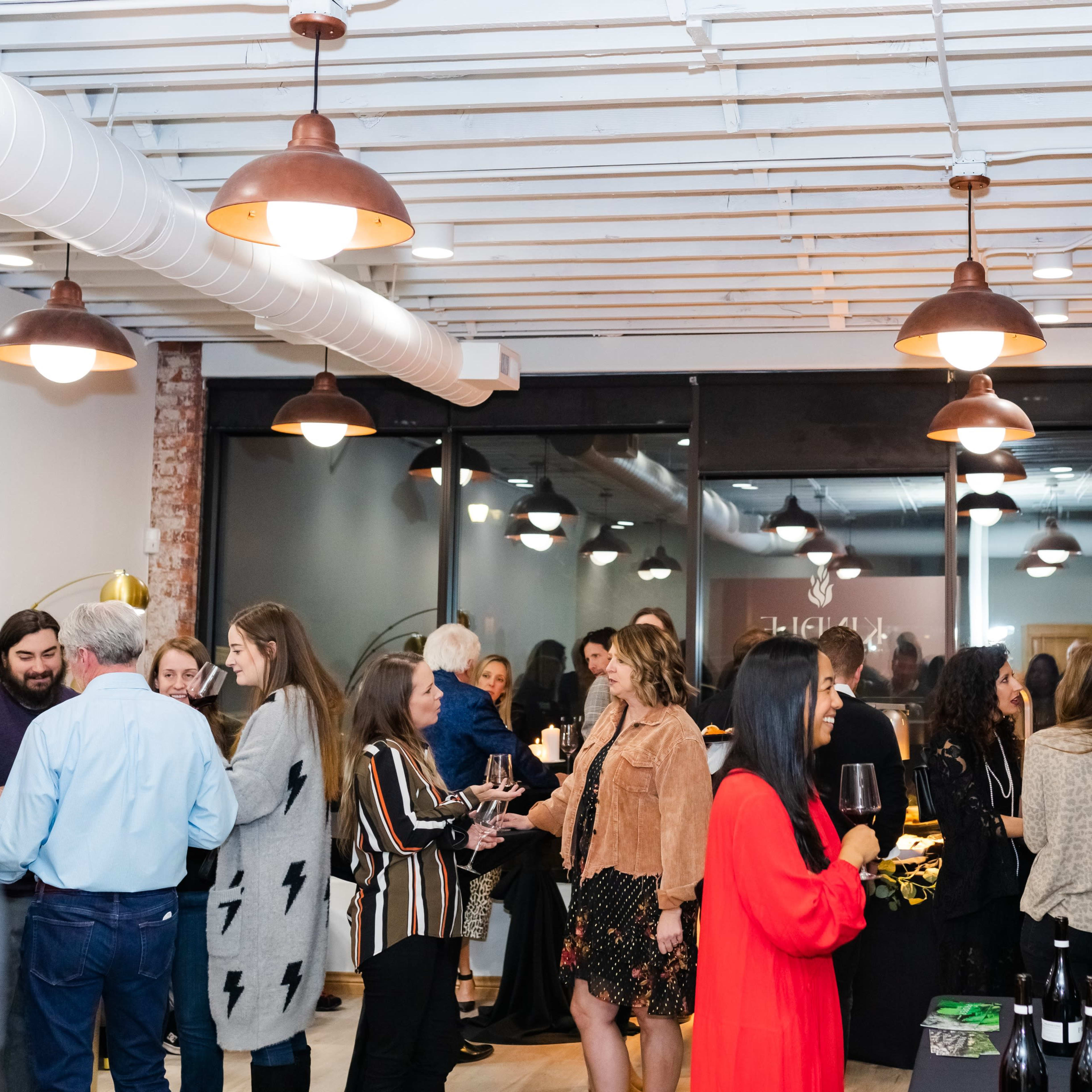A group of people engages in conversation and socializing at a gathering in a modern space with exposed brick walls and pendant lights.