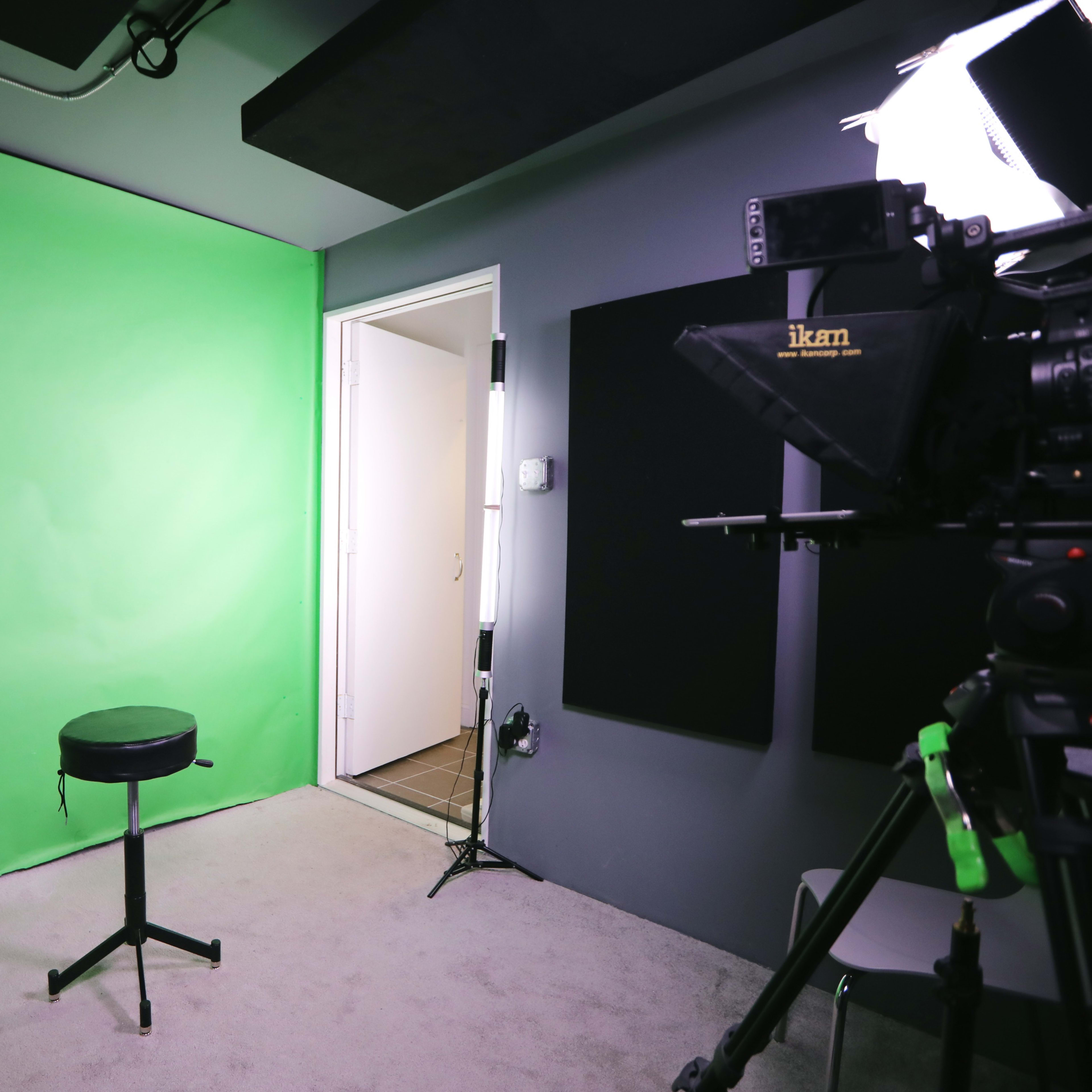 A green screen setup with a black stool in front, and a doorway visible in the background.