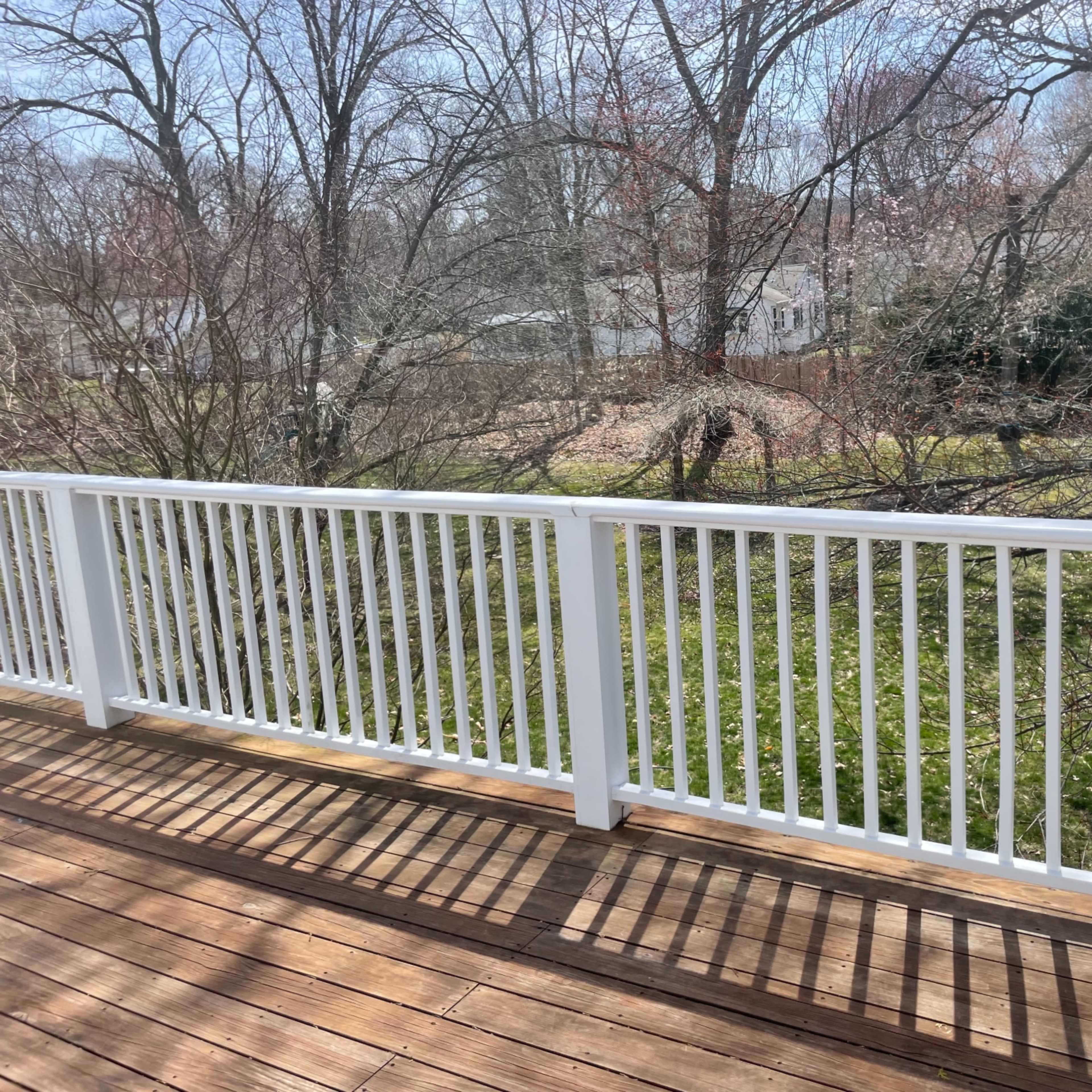 A wooden deck with a white railing overlooks a grassy yard shaded by leafless trees.
