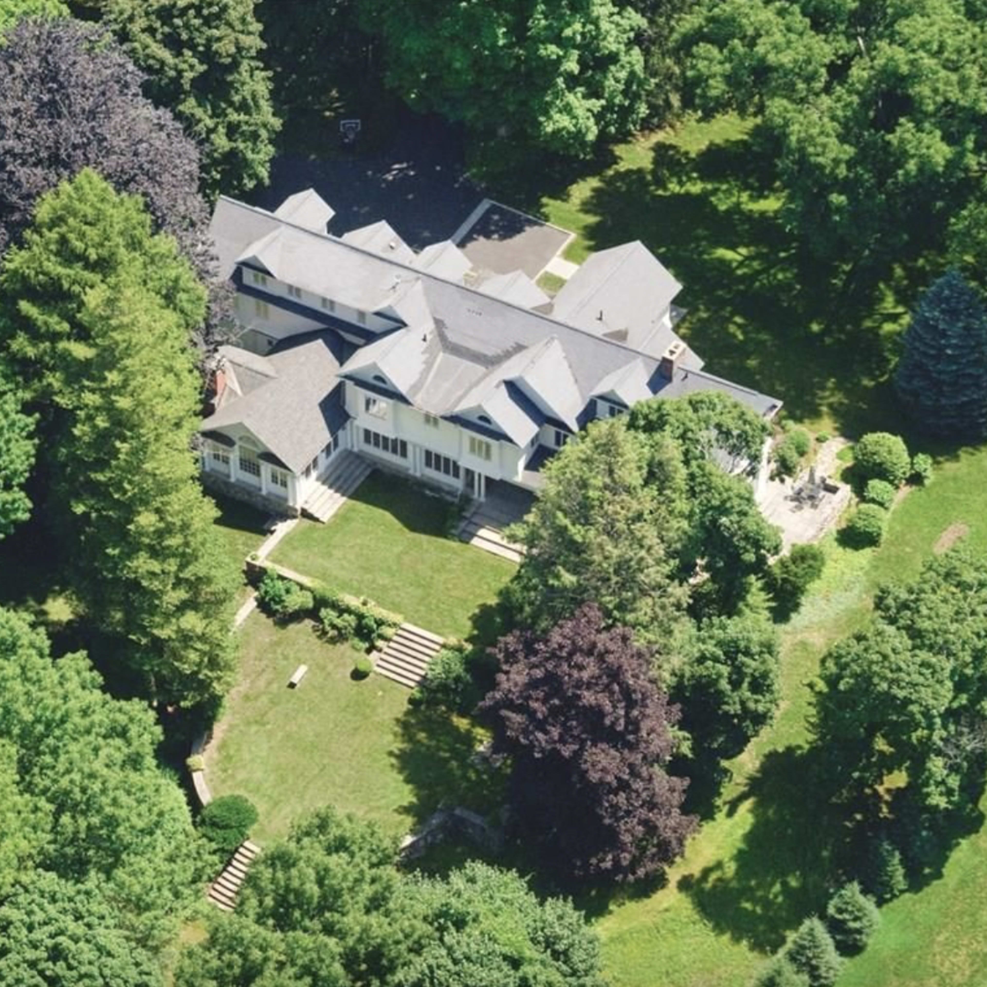A large house surrounded by dense trees and a well-maintained lawn.