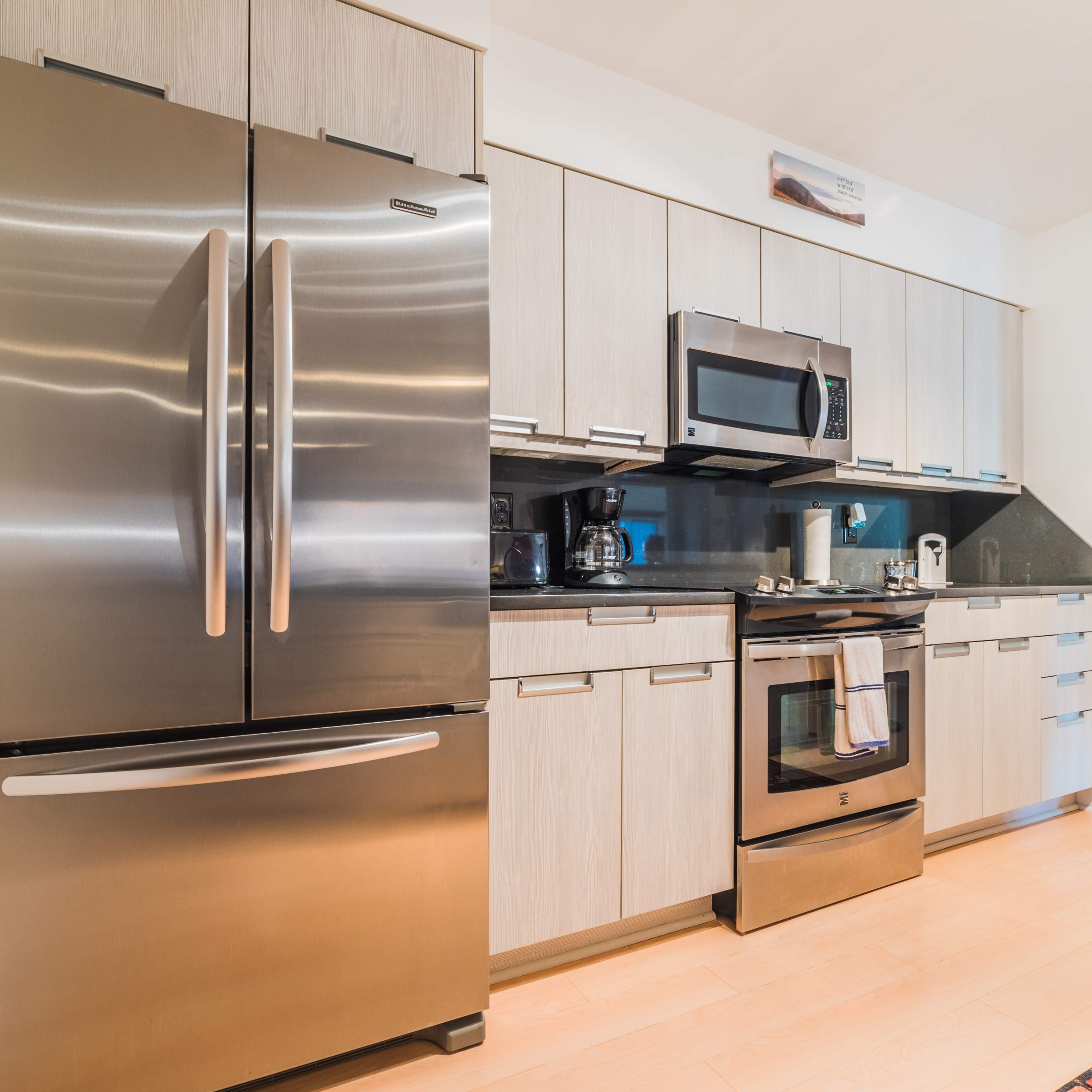 A modern kitchen with stainless steel appliances, including a refrigerator, microwave, and oven, alongside light wooden cabinetry.