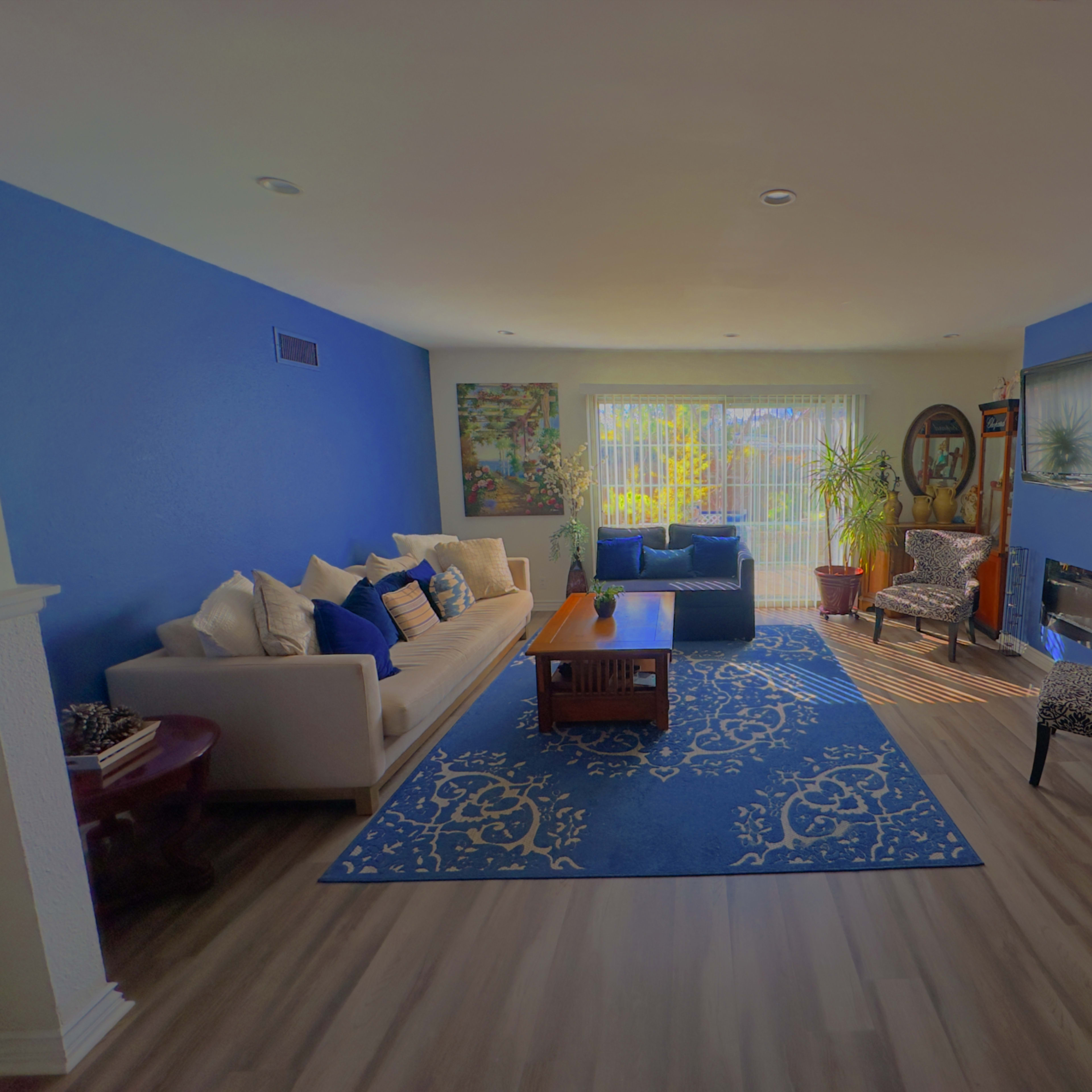 A living room with blue accent walls, a light-colored sofa, a patterned armchair, a coffee table, and a large window with natural light filtering in.