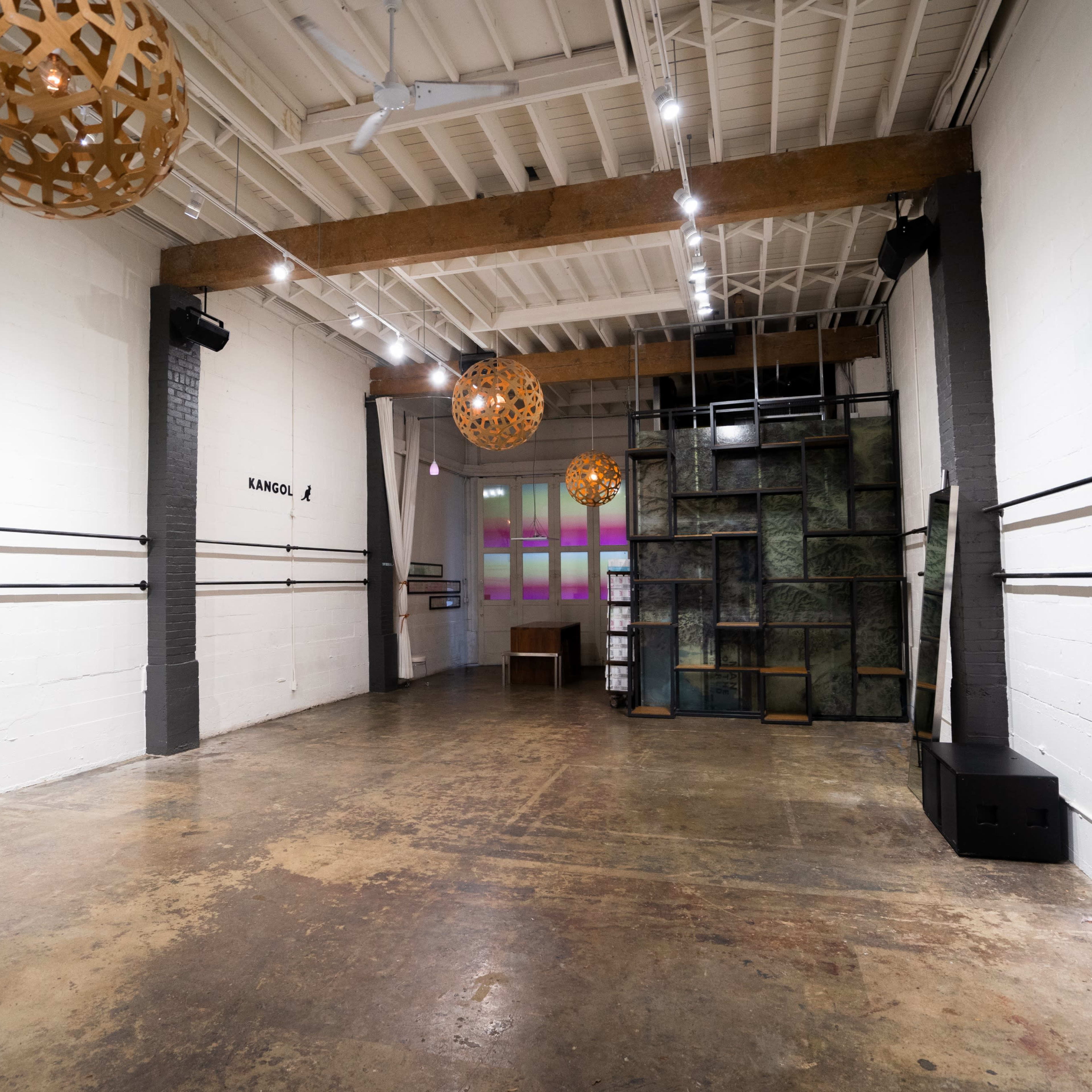 An empty industrial interior space with wooden beams, concrete walls, and decorative hanging lamps.