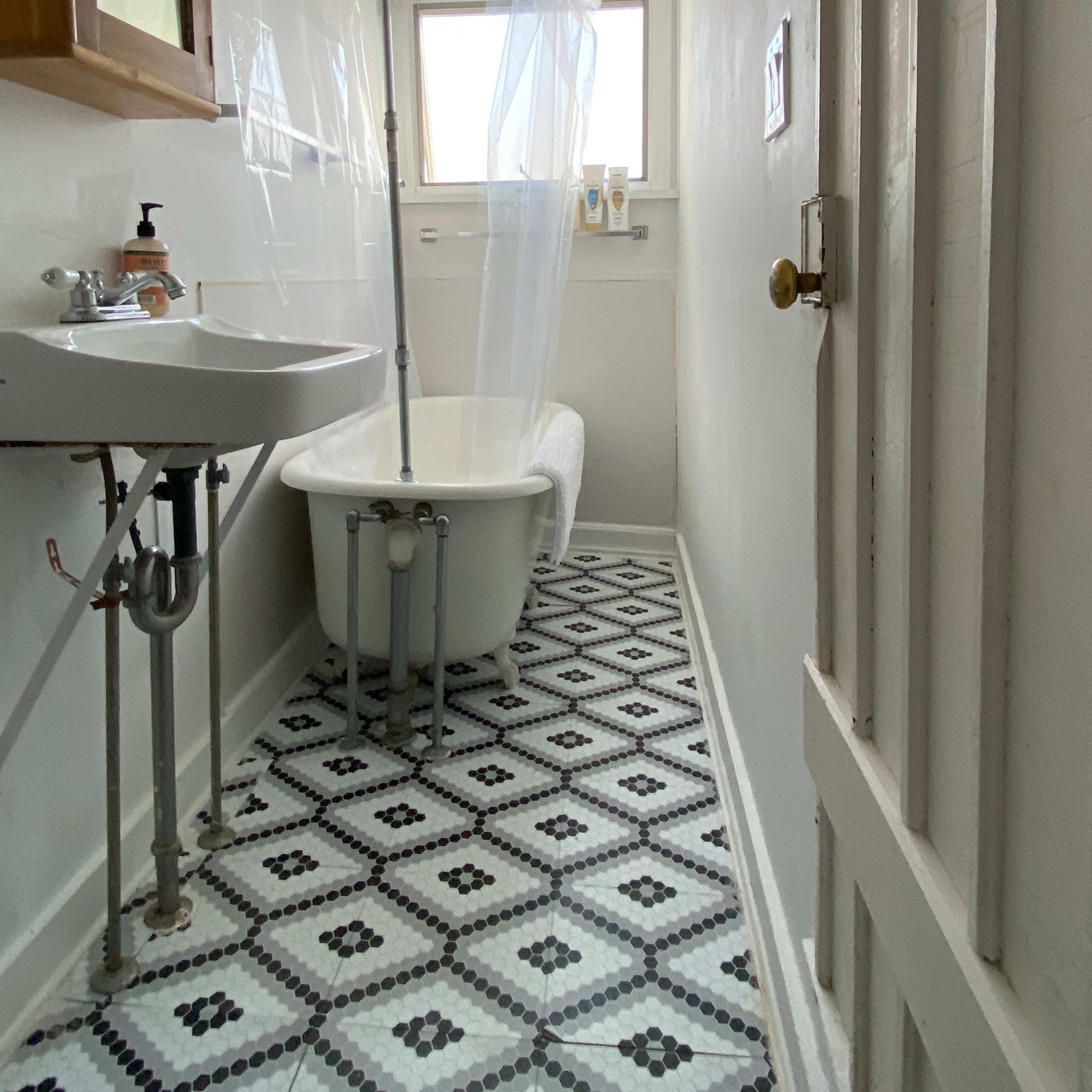 A small bathroom features a freestanding bathtub, a sink with a mirror, and patterned tile flooring.