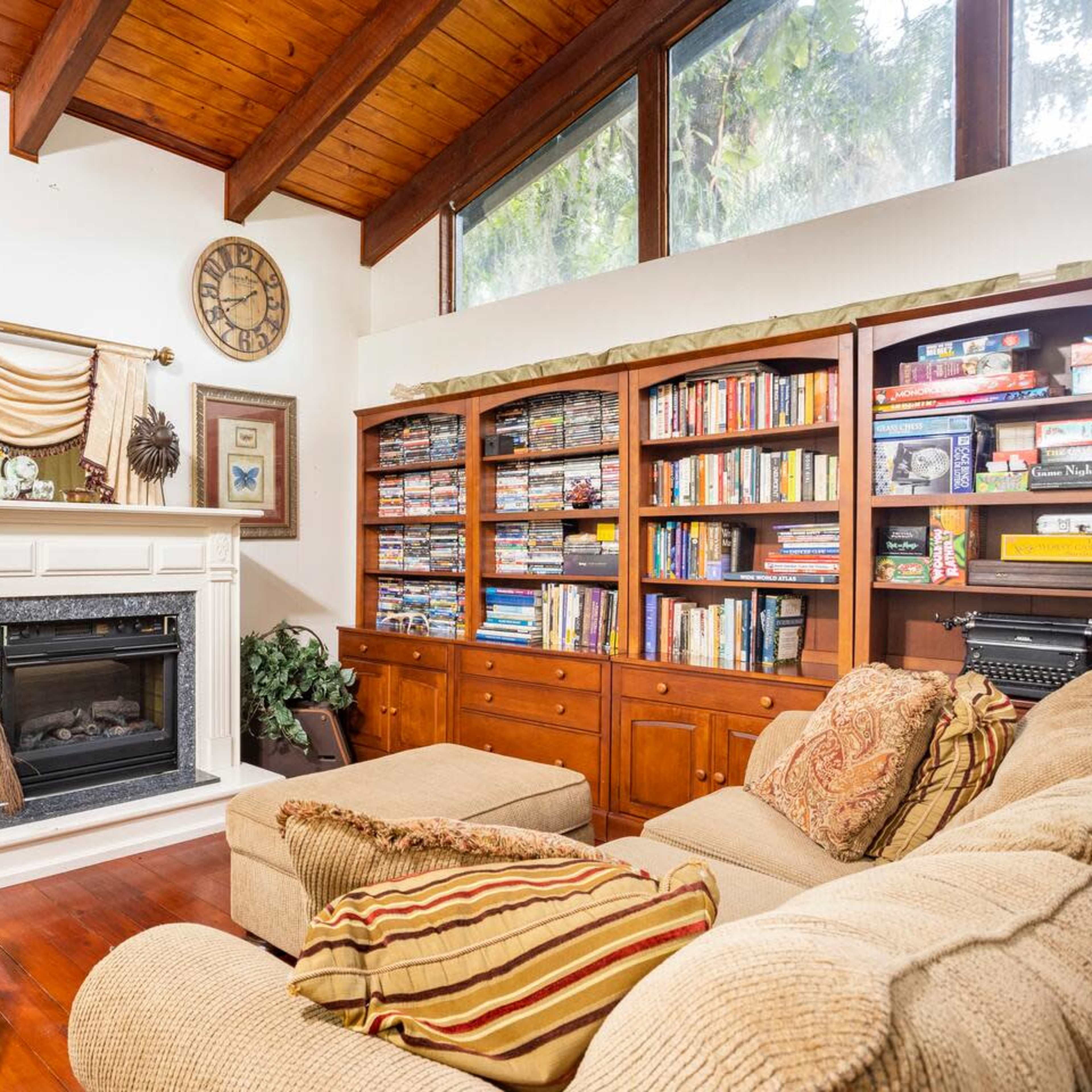 A cozy living room featuring a fireplace, a large bookshelf filled with books and games, and comfortable seating arranged around a coffee table.