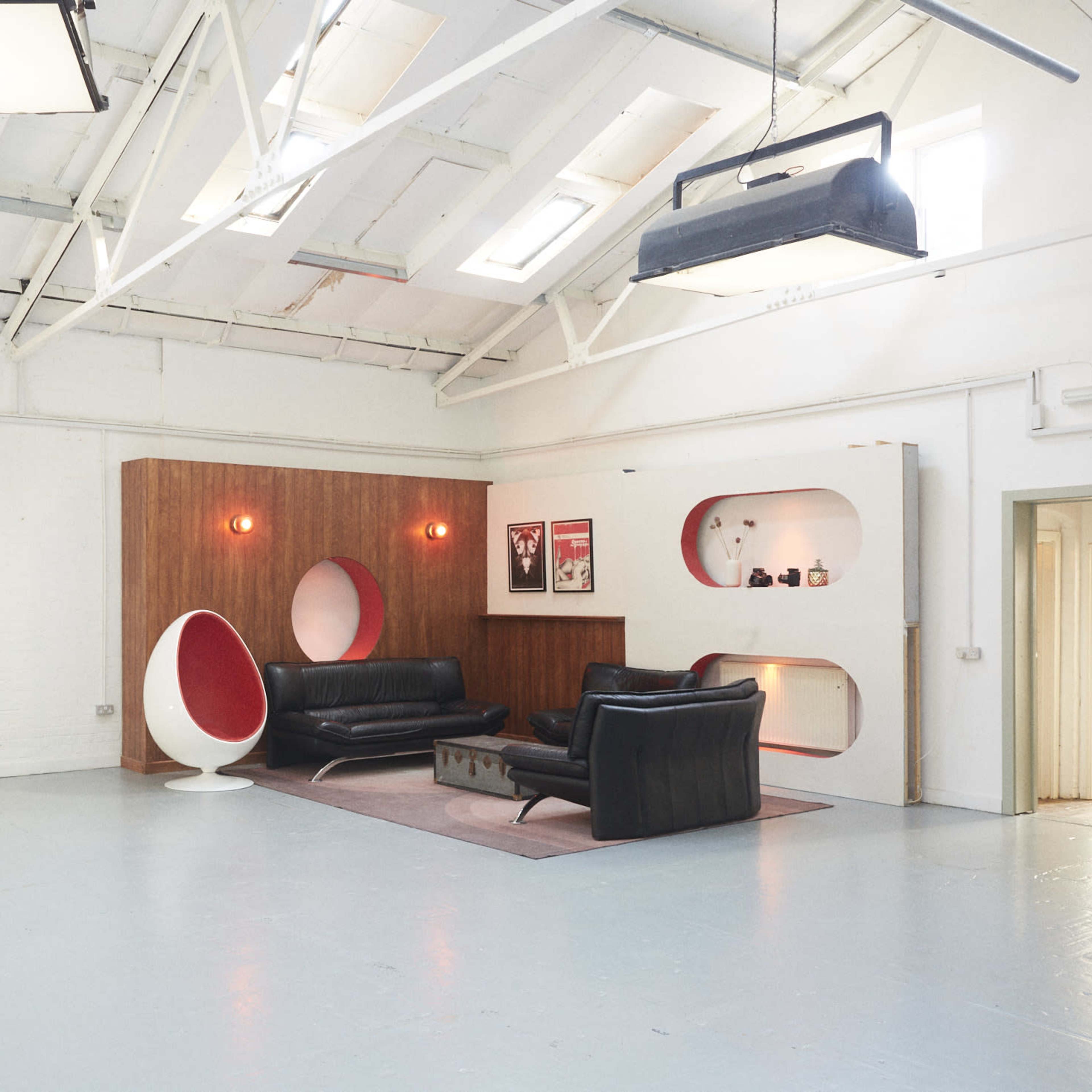 A spacious interior with a modern design, featuring a black leather sofa, a stylized white egg chair, and decorative wall niches with lighting.