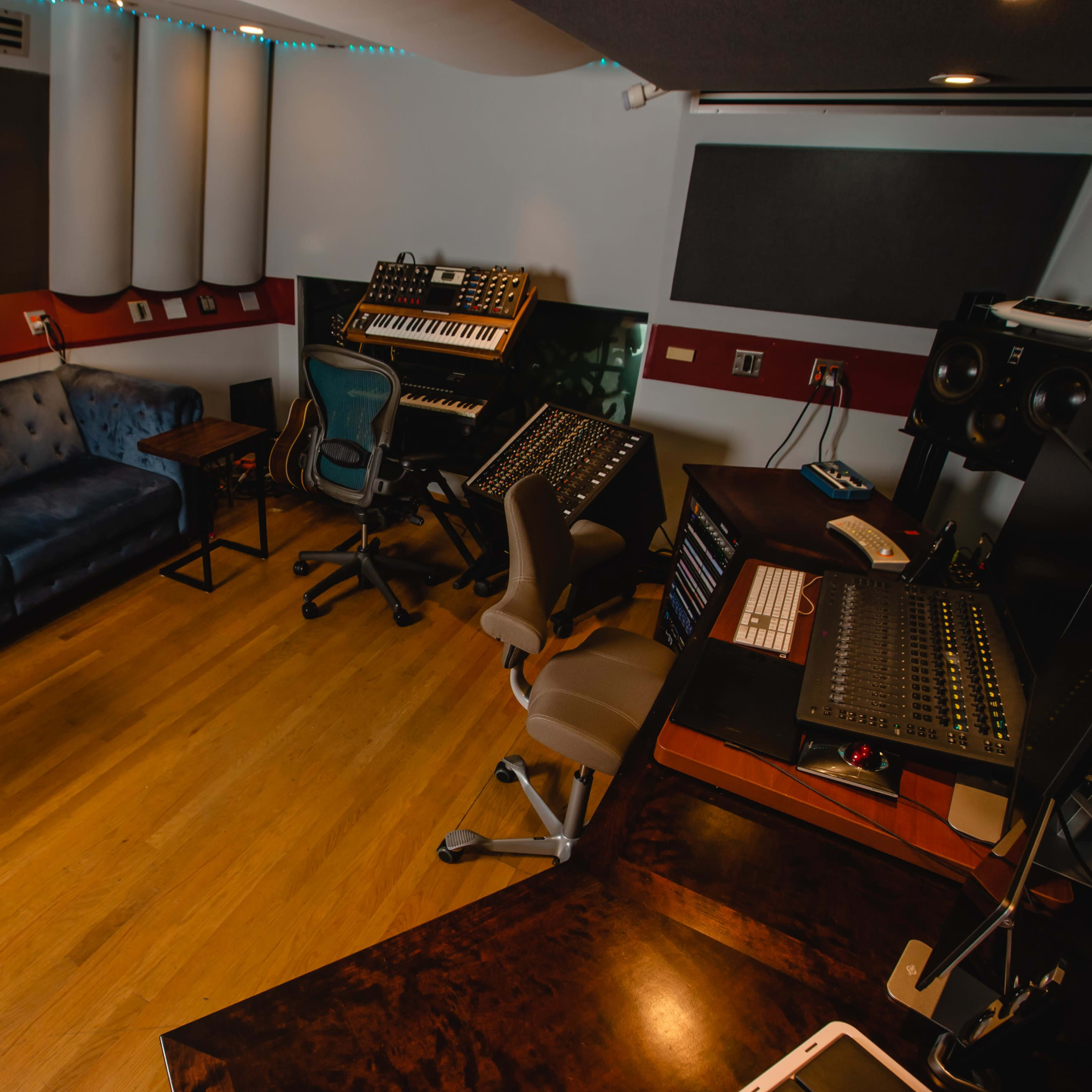 A music studio with a blue sofa, wooden table, and various sound equipment arranged around the room.