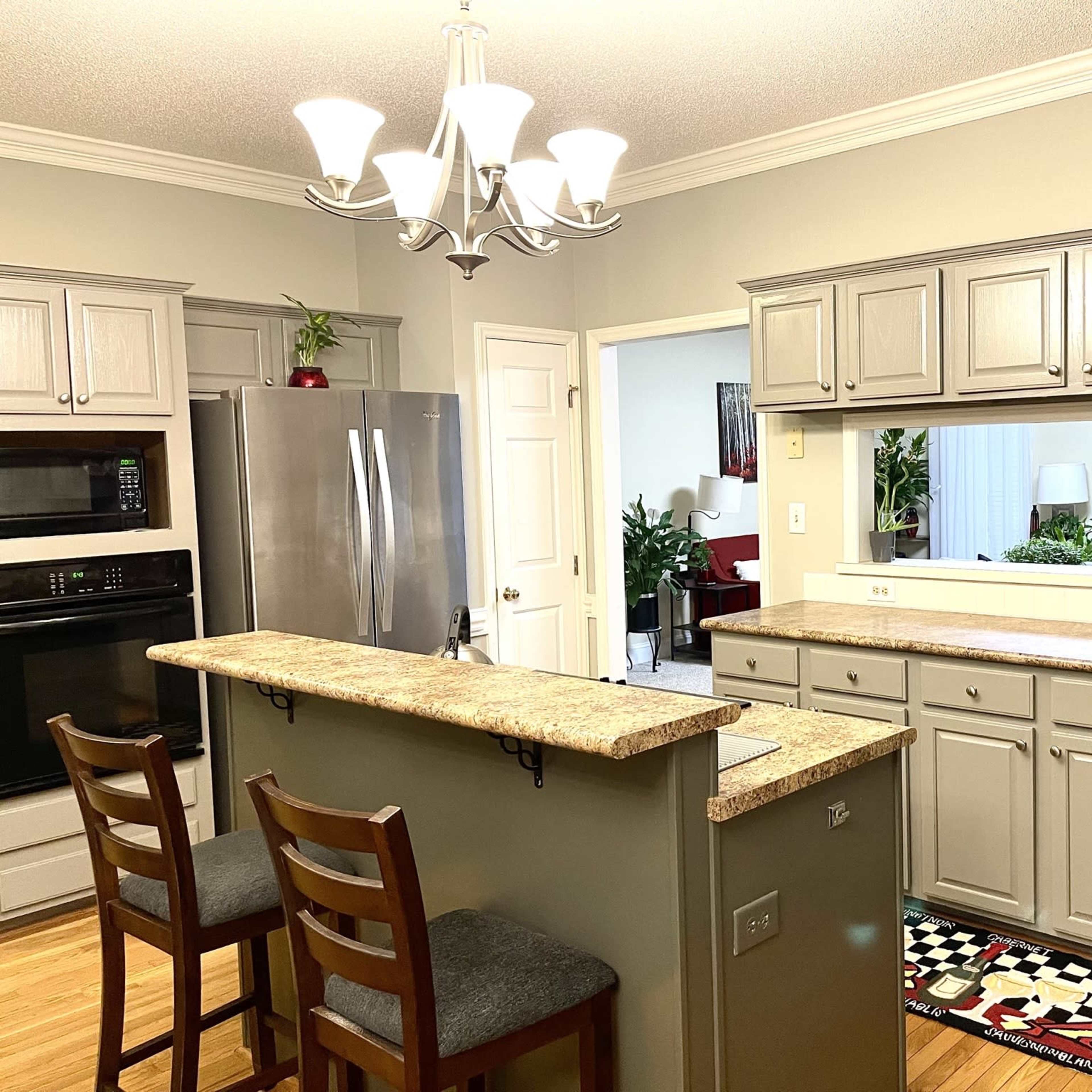 A modern kitchen features gray cabinets, stainless steel appliances, and a granite island with two bar stools.