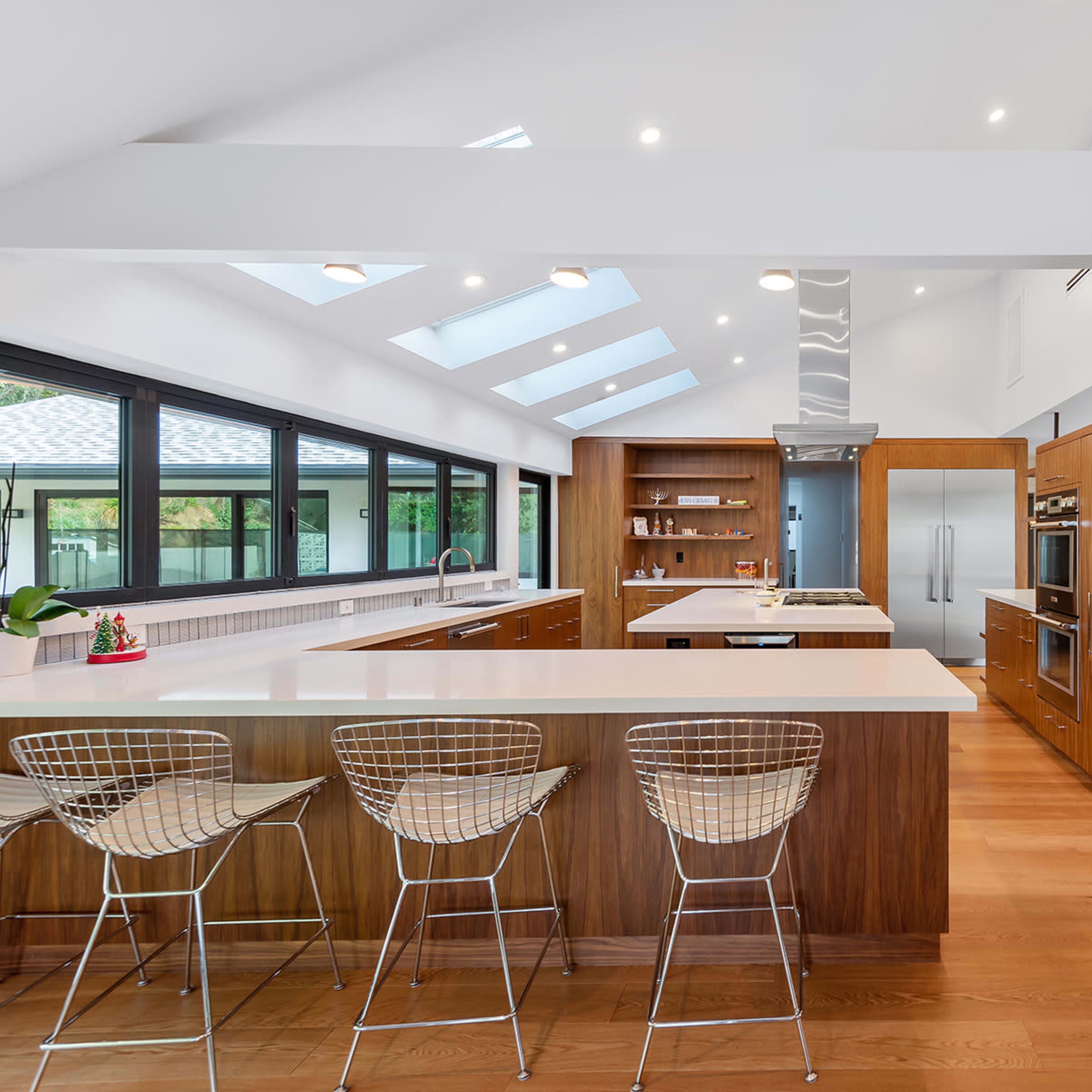 A modern kitchen with wooden cabinetry, an island with bar stools, and skylights illuminating the space.