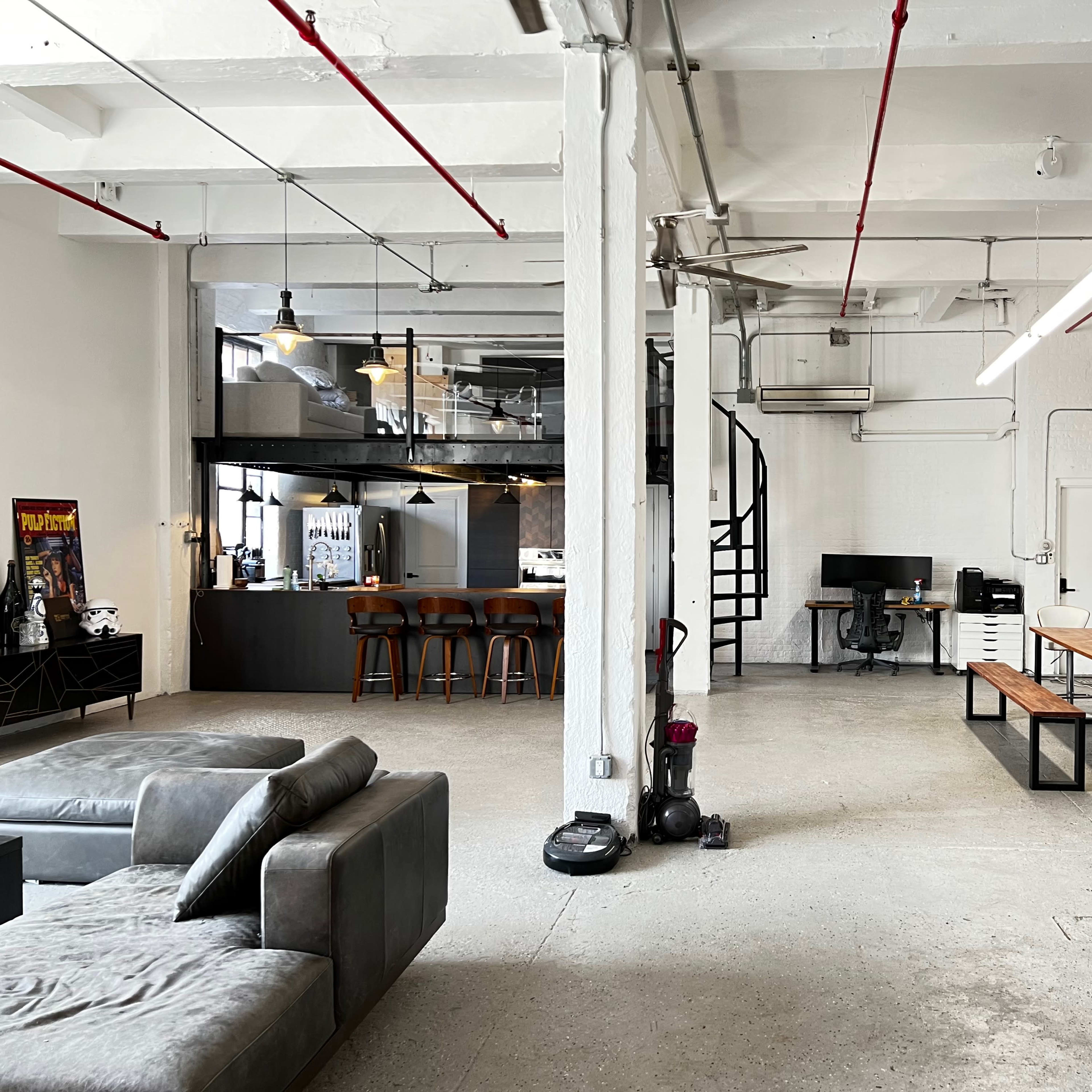 A spacious, modern open-concept office with a seating area, dining table, and a kitchen in the background.