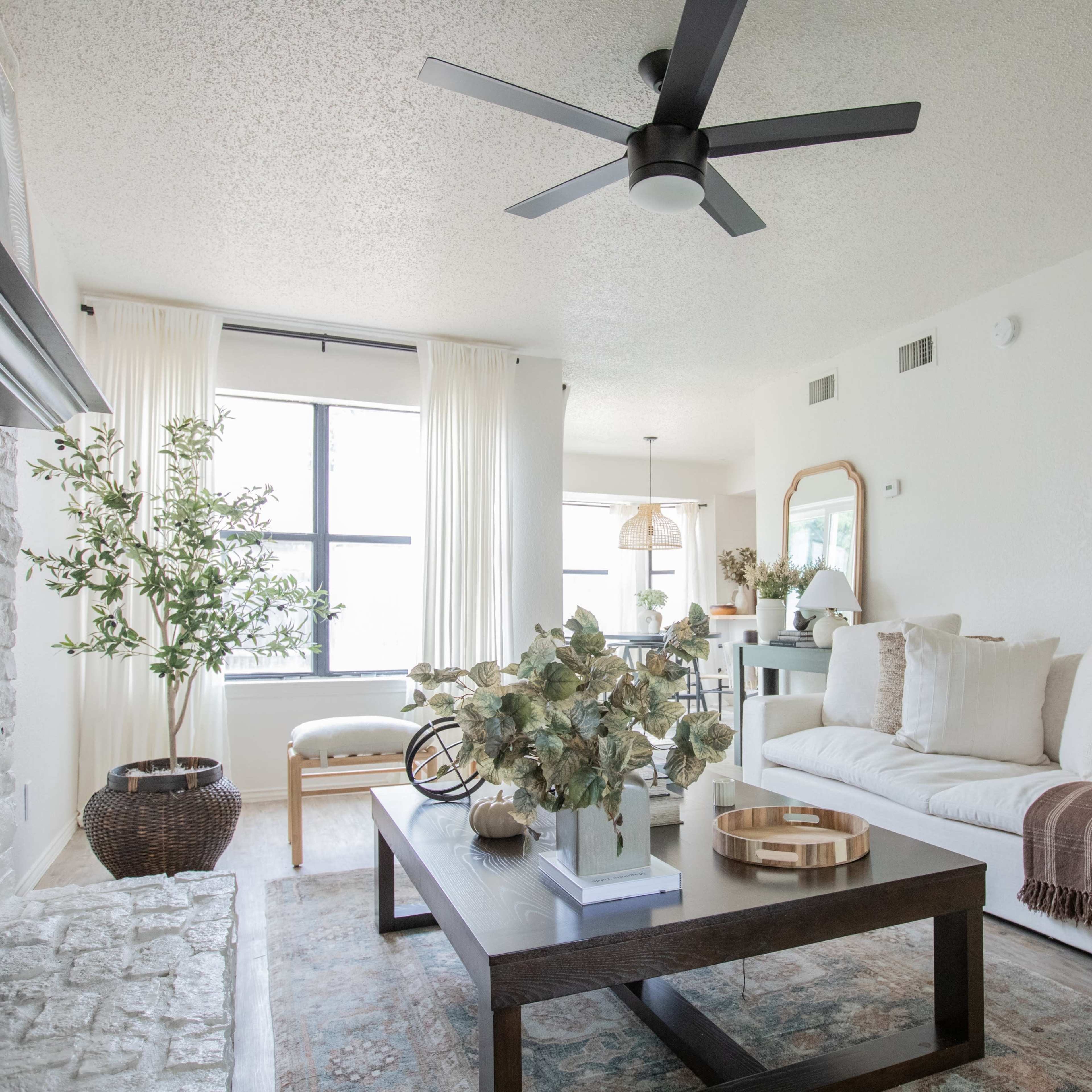 A modern living room with a light-colored sofa, a coffee table, and large windows letting in natural light.