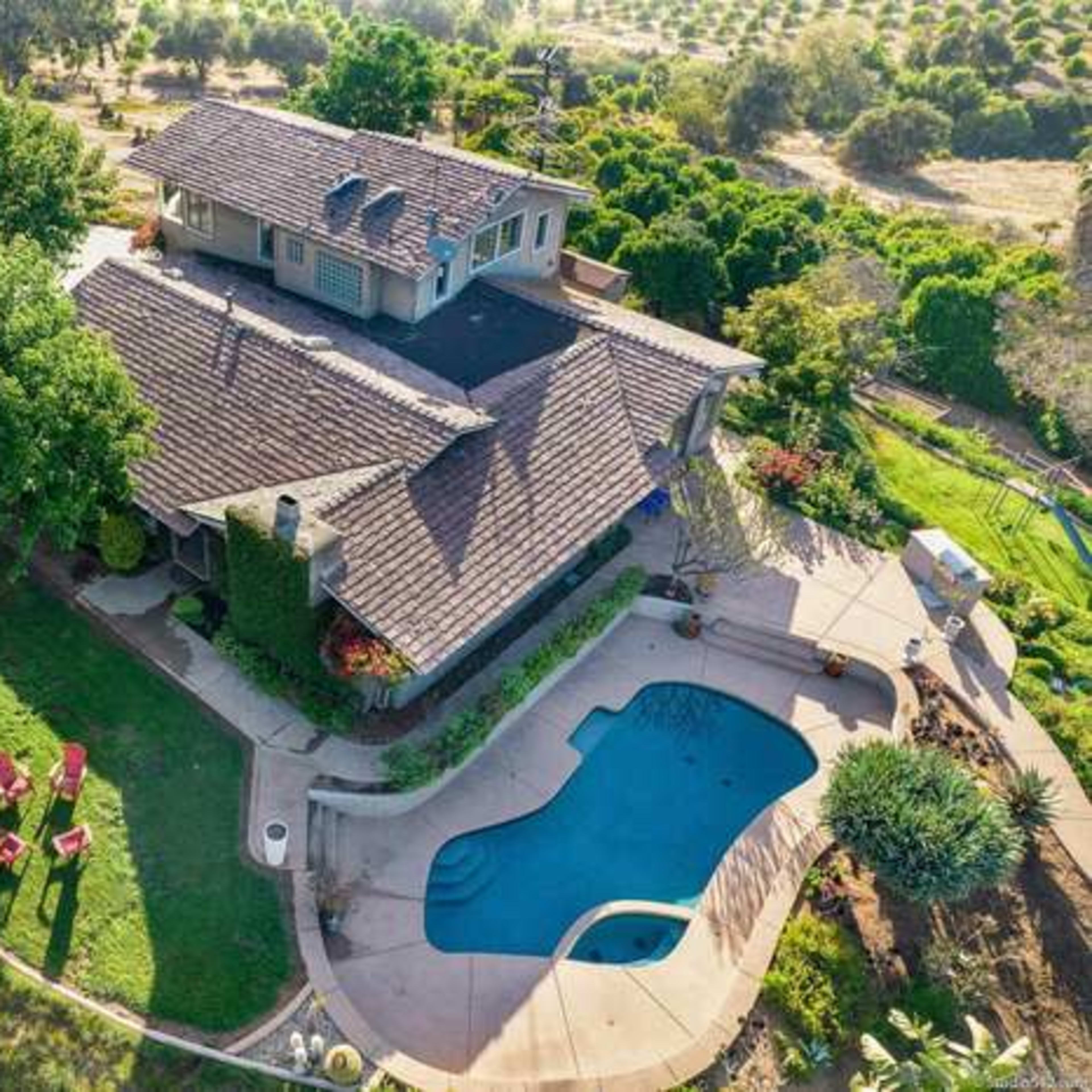 A two-story house with a pool and lounge chairs, surrounded by lush greenery and trees.