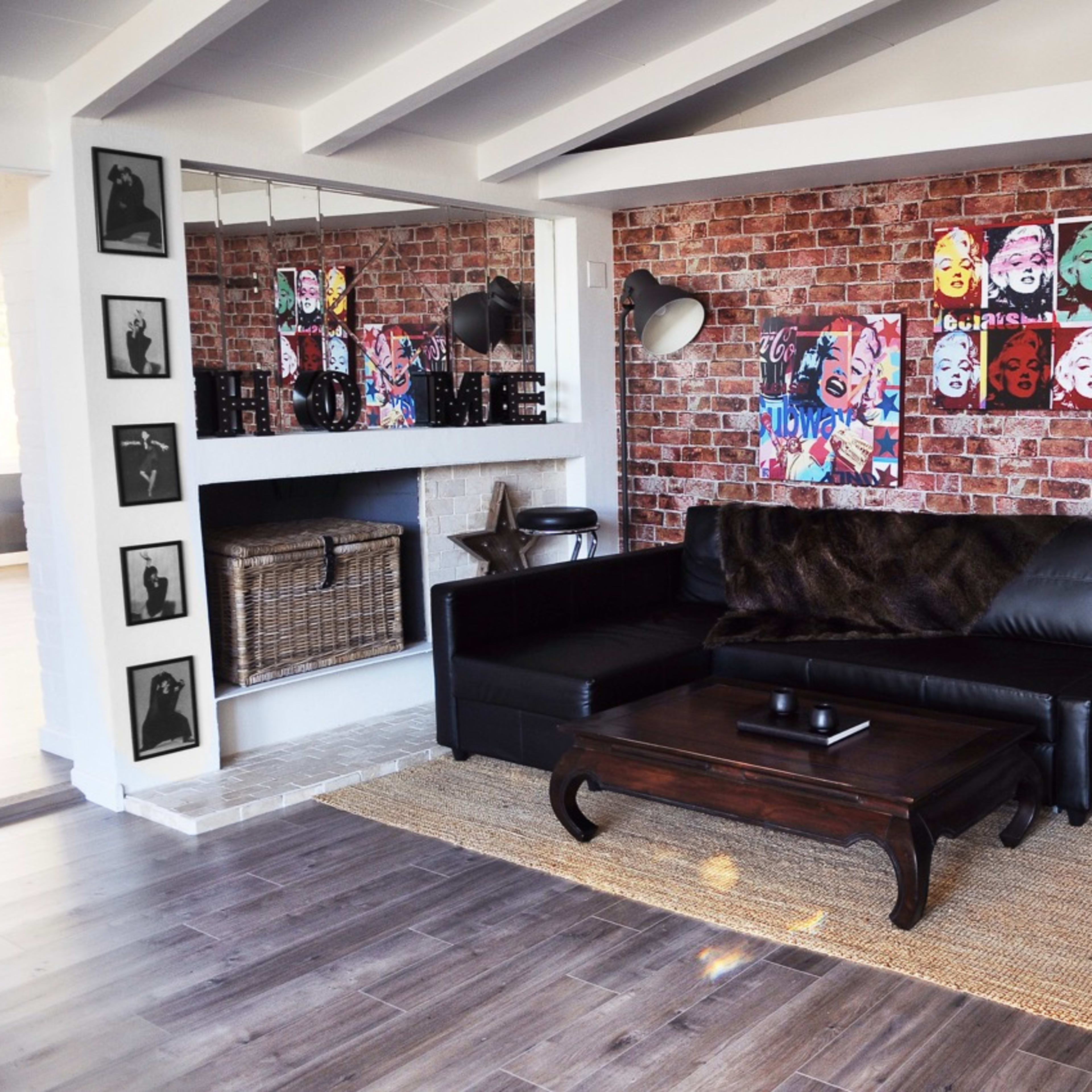 A modern living room with a dark leather sofa, a wooden coffee table, and a textured brick wall adorned with colorful artwork and framed photographs.