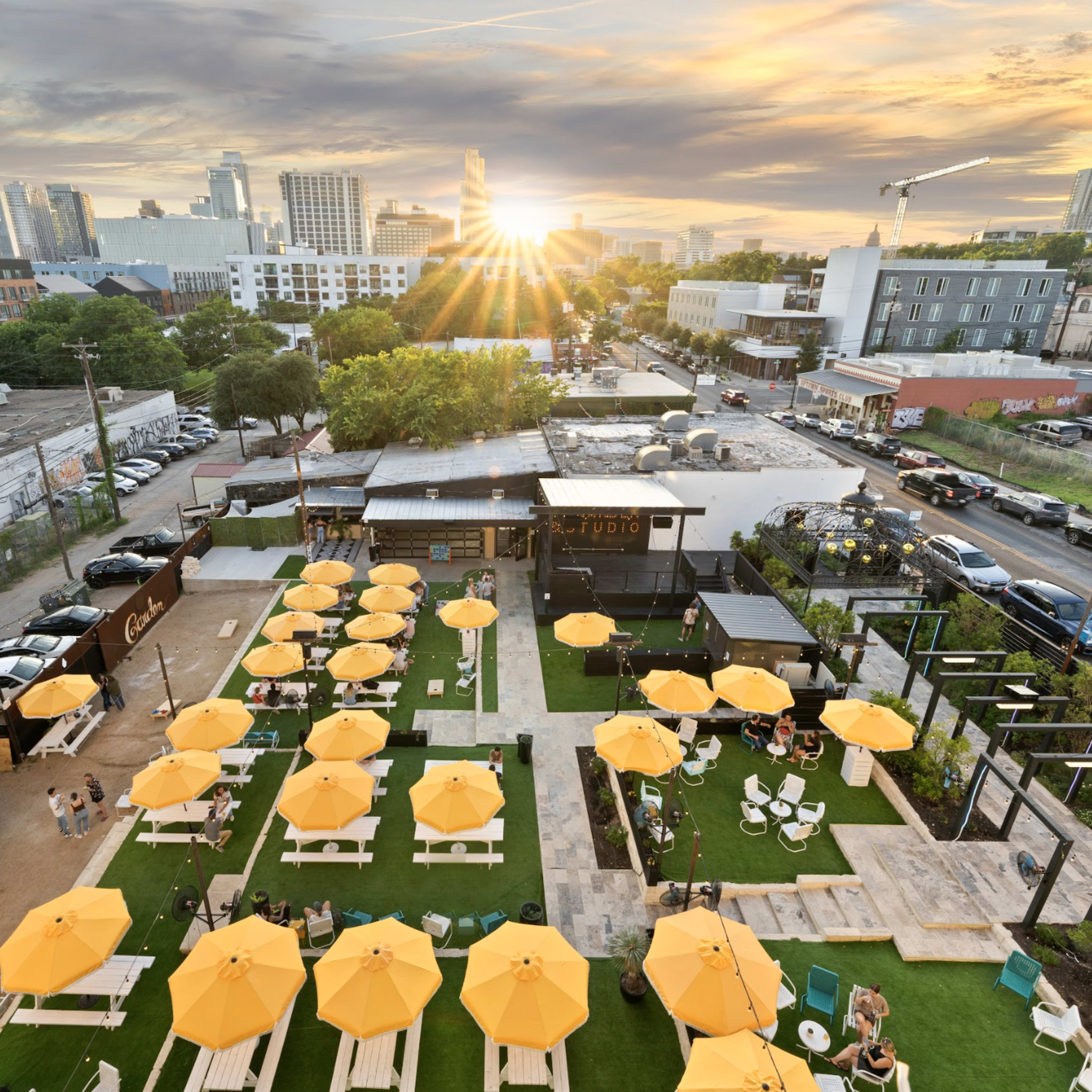A rooftop venue with yellow umbrellas covering outdoor seating, surrounded by city skyline and sunset in the background.