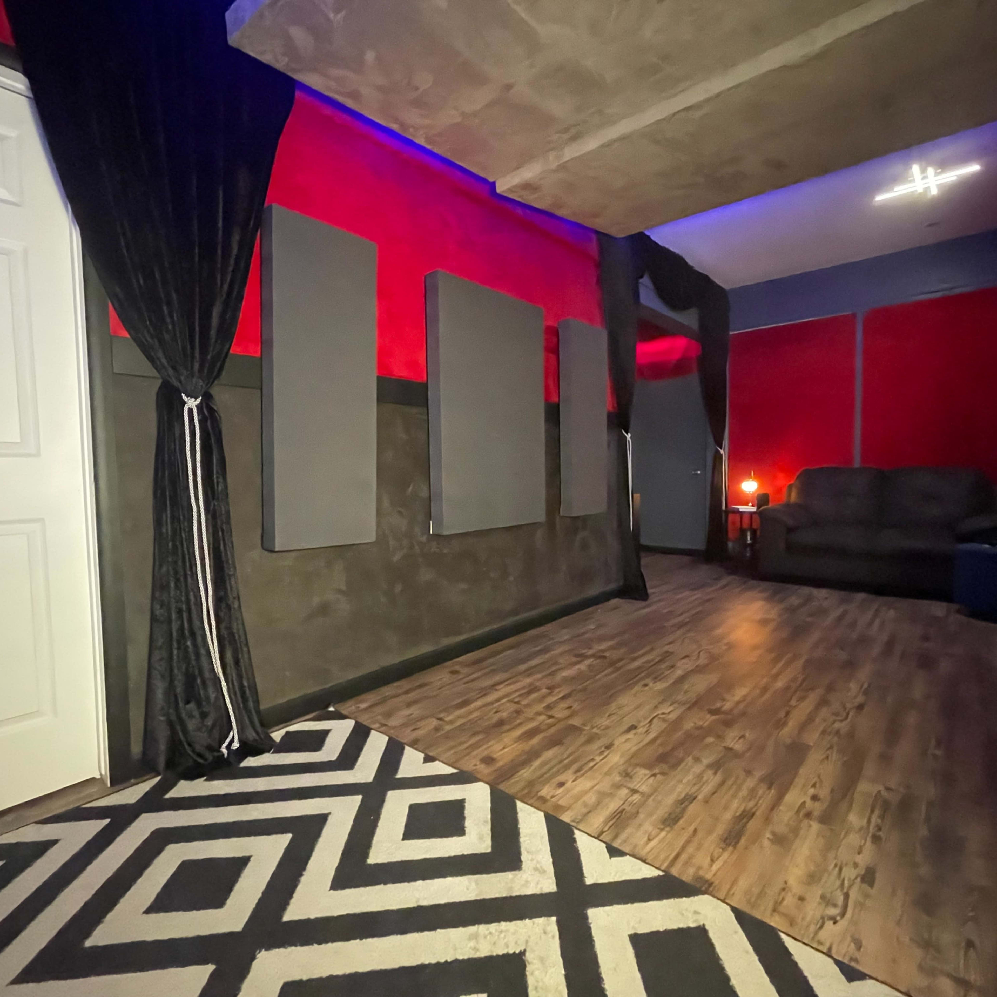 A room with red walls, acoustic panels, a dark couch, and a patterned rug.