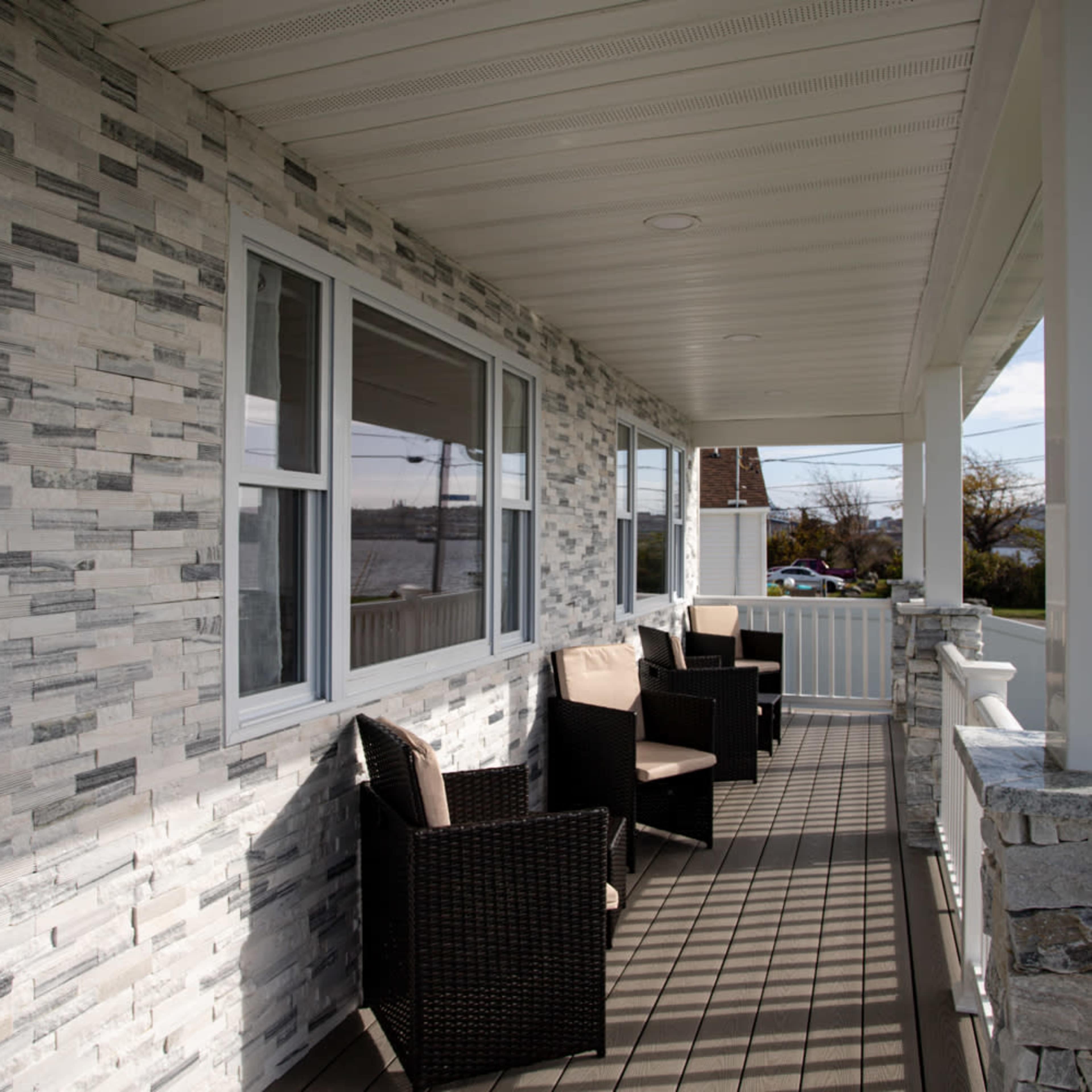A covered porch with woven chairs and a stone-clad wall overlooking a body of water.