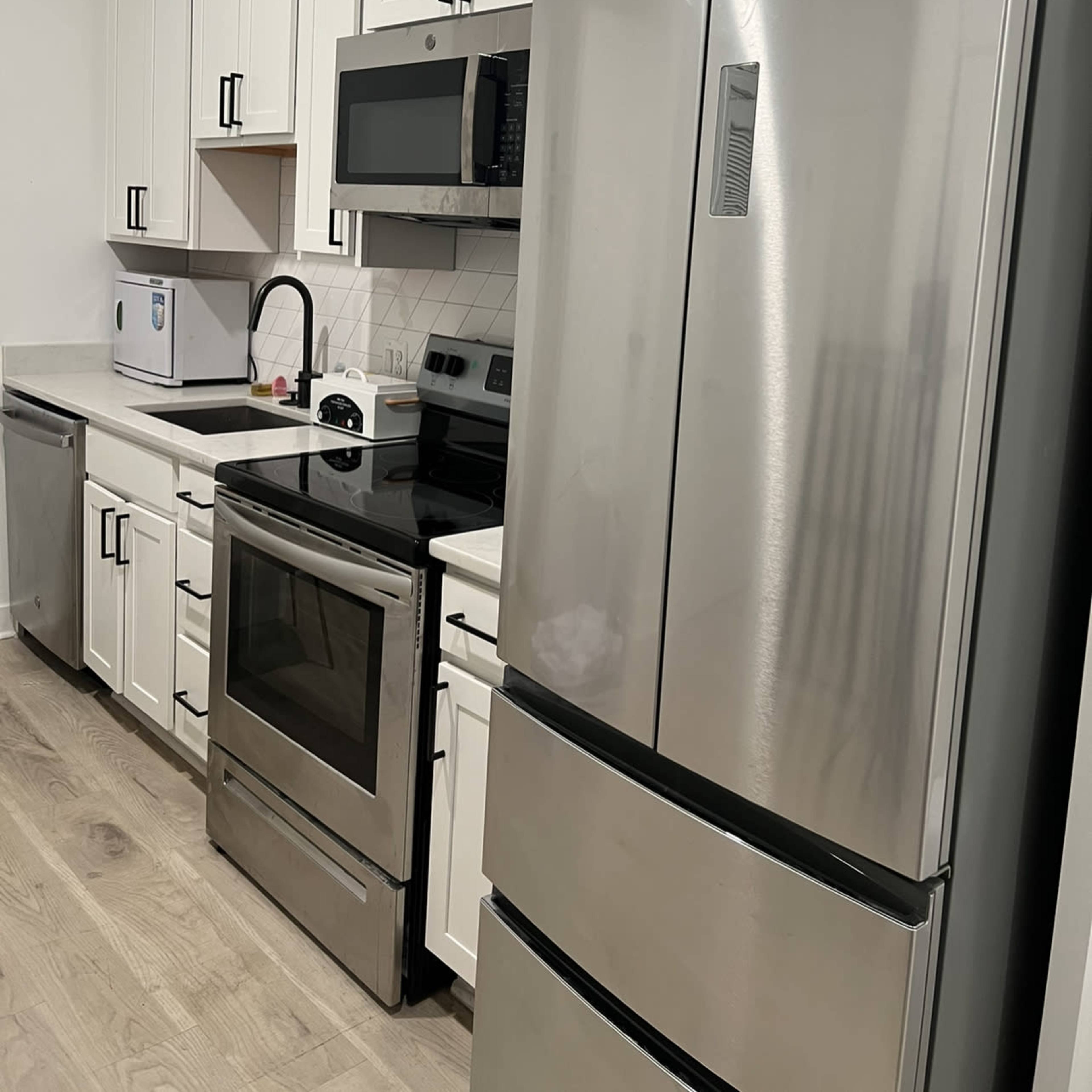 A modern kitchen featuring white cabinets, stainless steel appliances, and a countertop with a sink and microwave.