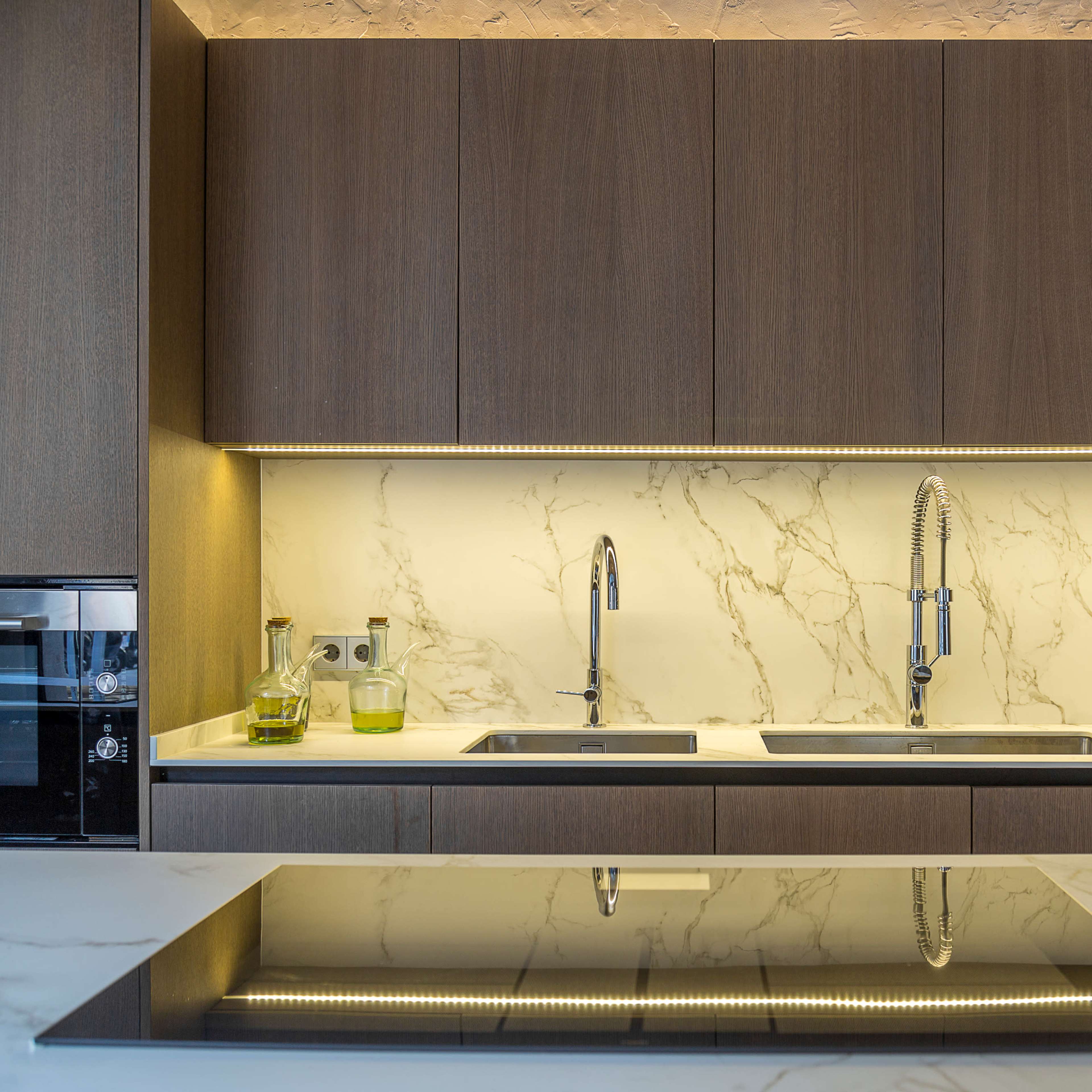 A modern kitchen with dark cabinetry, a marble backsplash, dual sinks, and a stovetop island.
