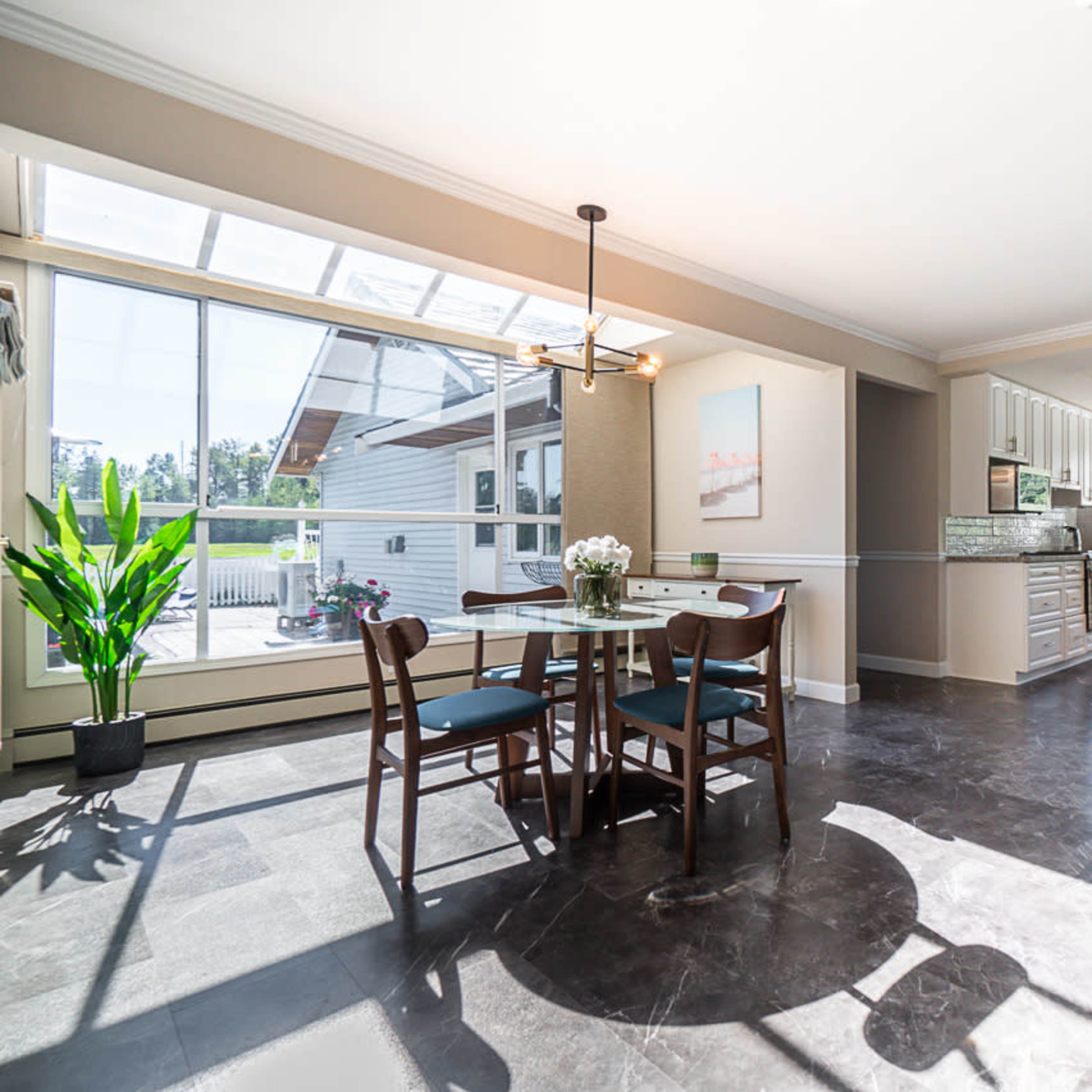 A modern kitchen and dining area with a glass door leading to an outdoor space, featuring a round table with chairs and a bar counter.