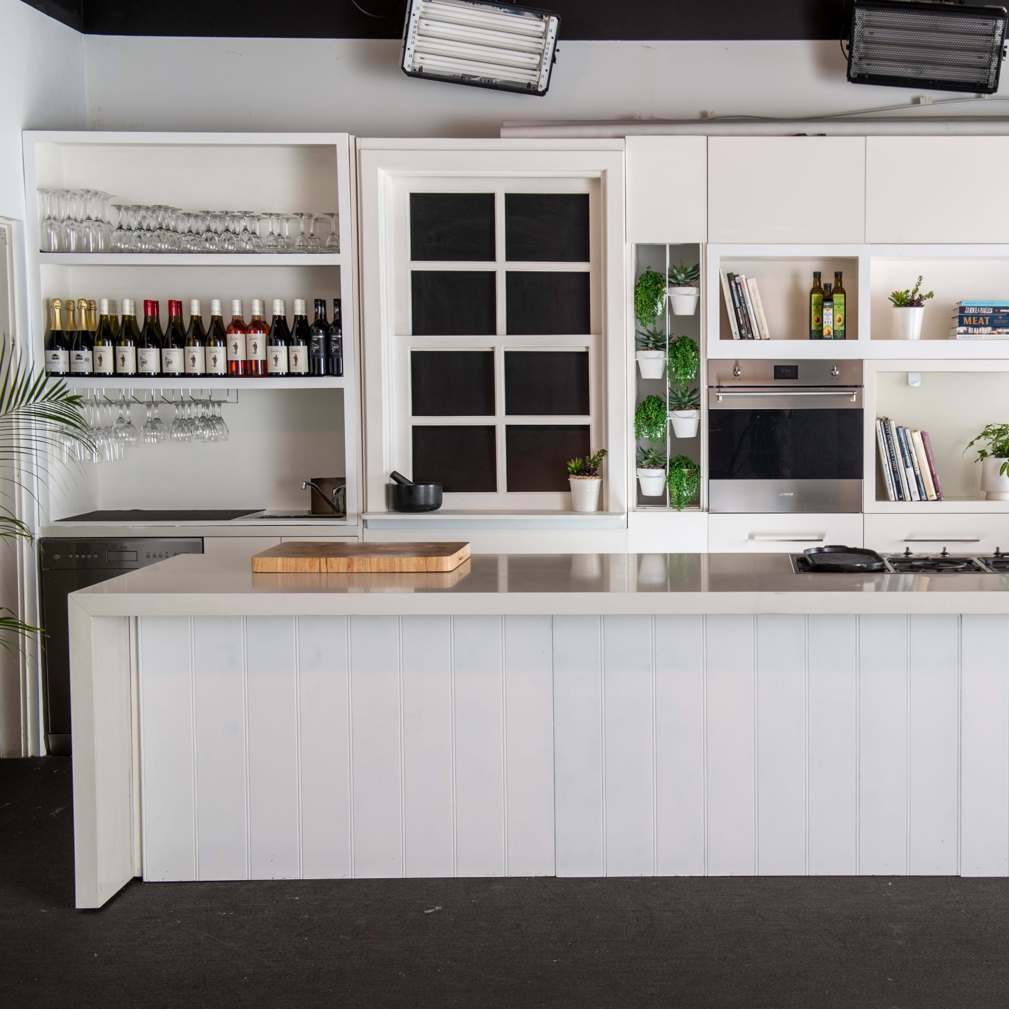 A modern kitchen with a large white island, built-in appliances, shelves holding glassware and bottles, and minimalist decor.