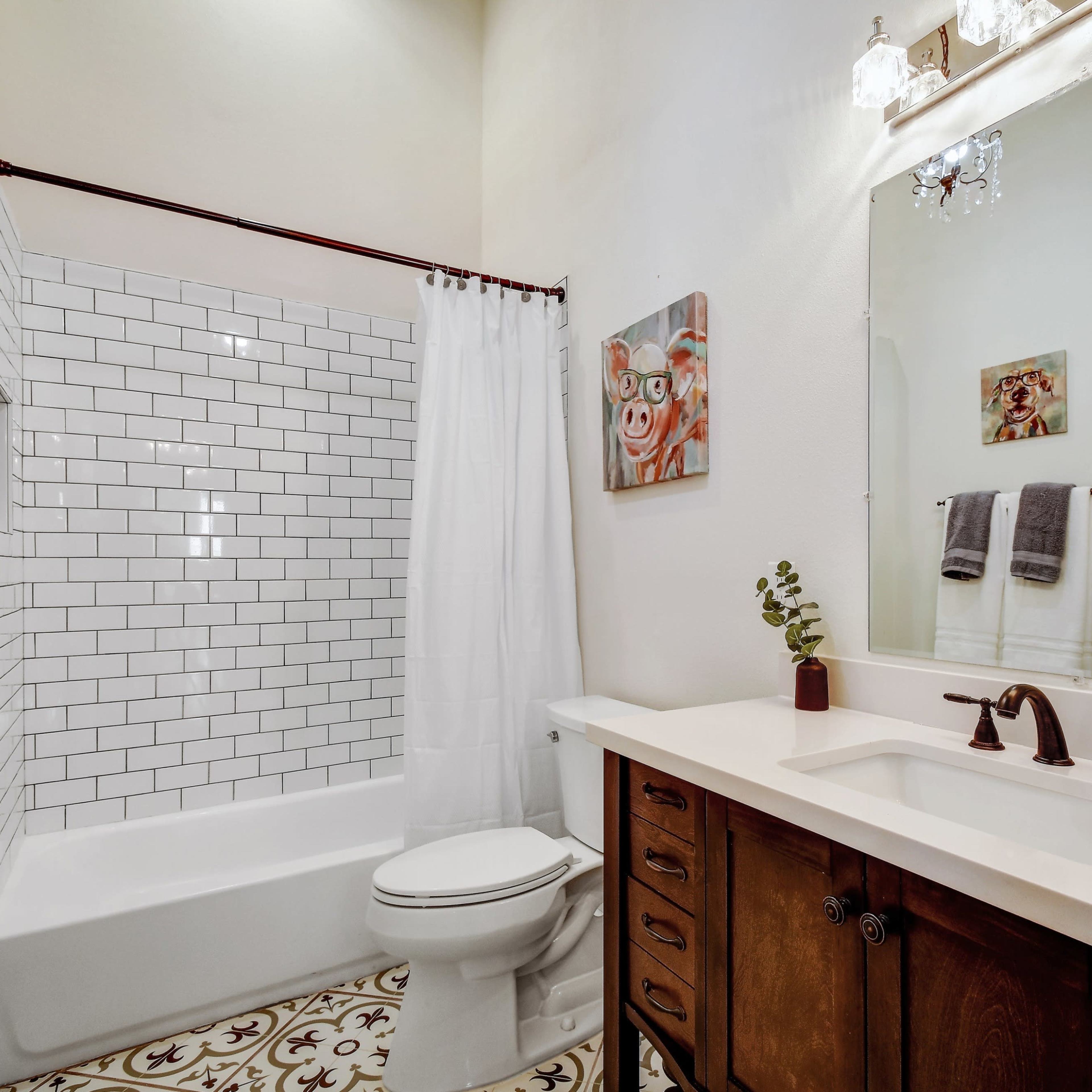 A bathroom featuring a white tiled shower, a dual-sink vanity with wooden cabinetry, and decorative artwork on the walls.