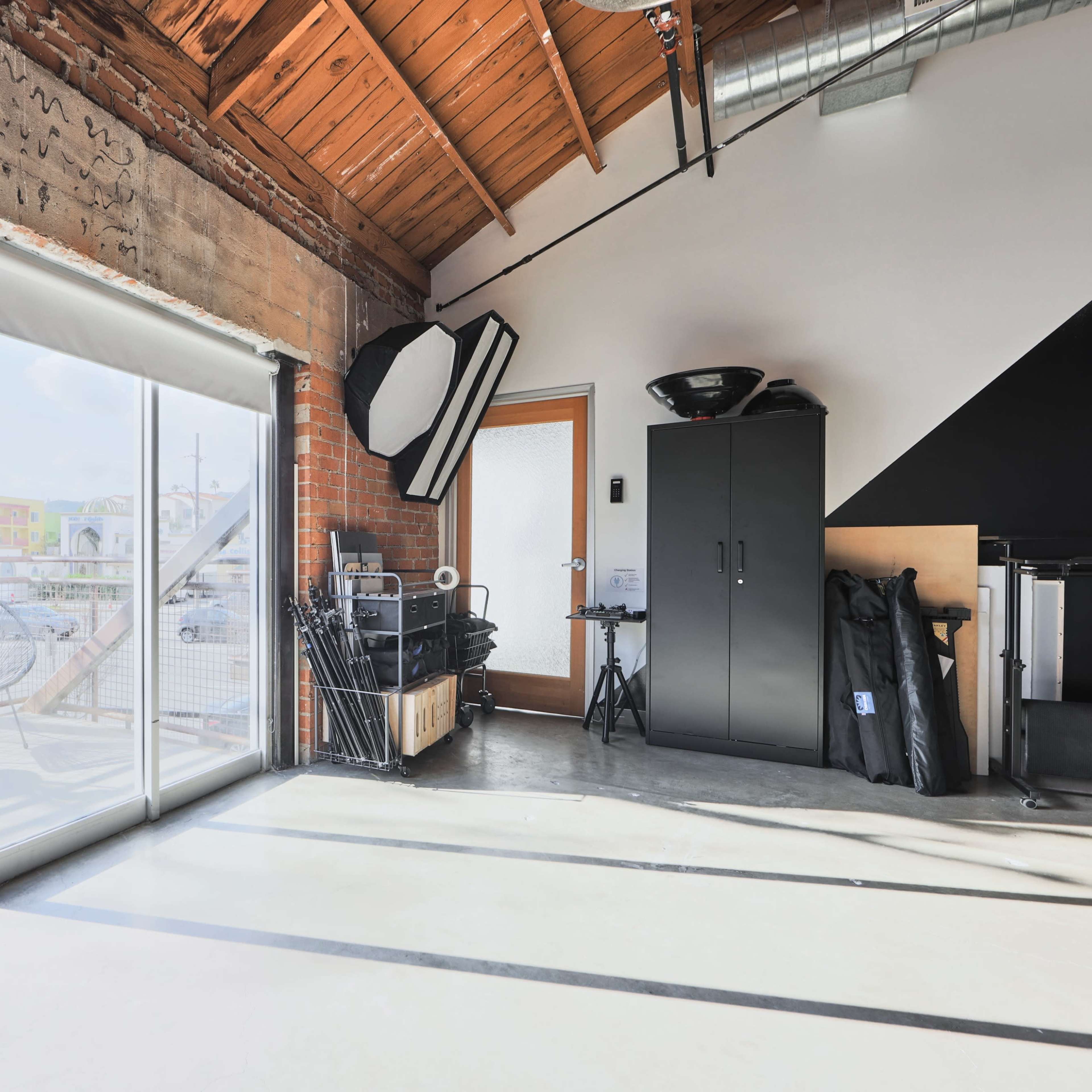 A spacious room with large sliding glass doors leading to a balcony, featuring a wooden ceiling and minimalist furniture.