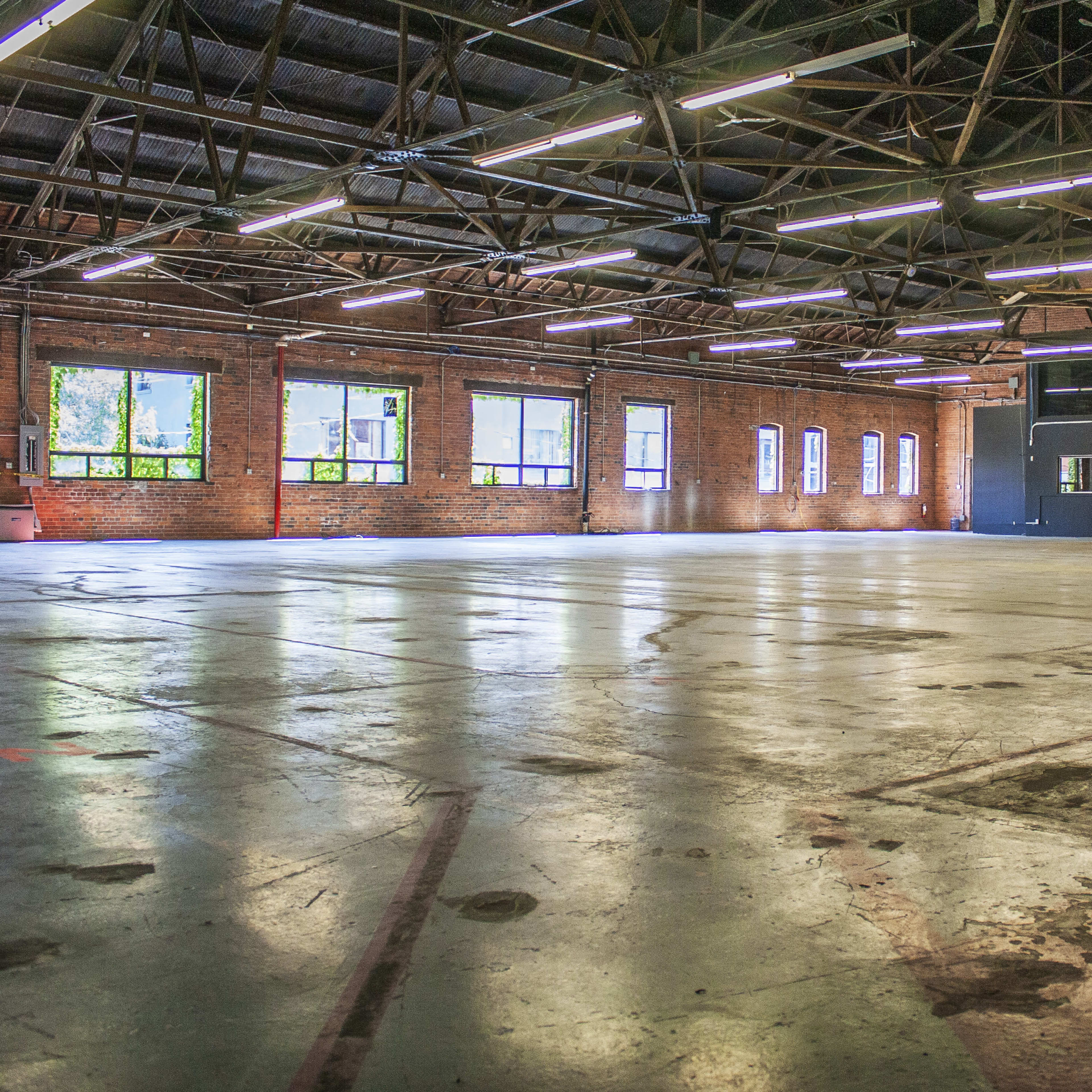 A large, empty industrial space with exposed brick walls, large windows, and a polished concrete floor.