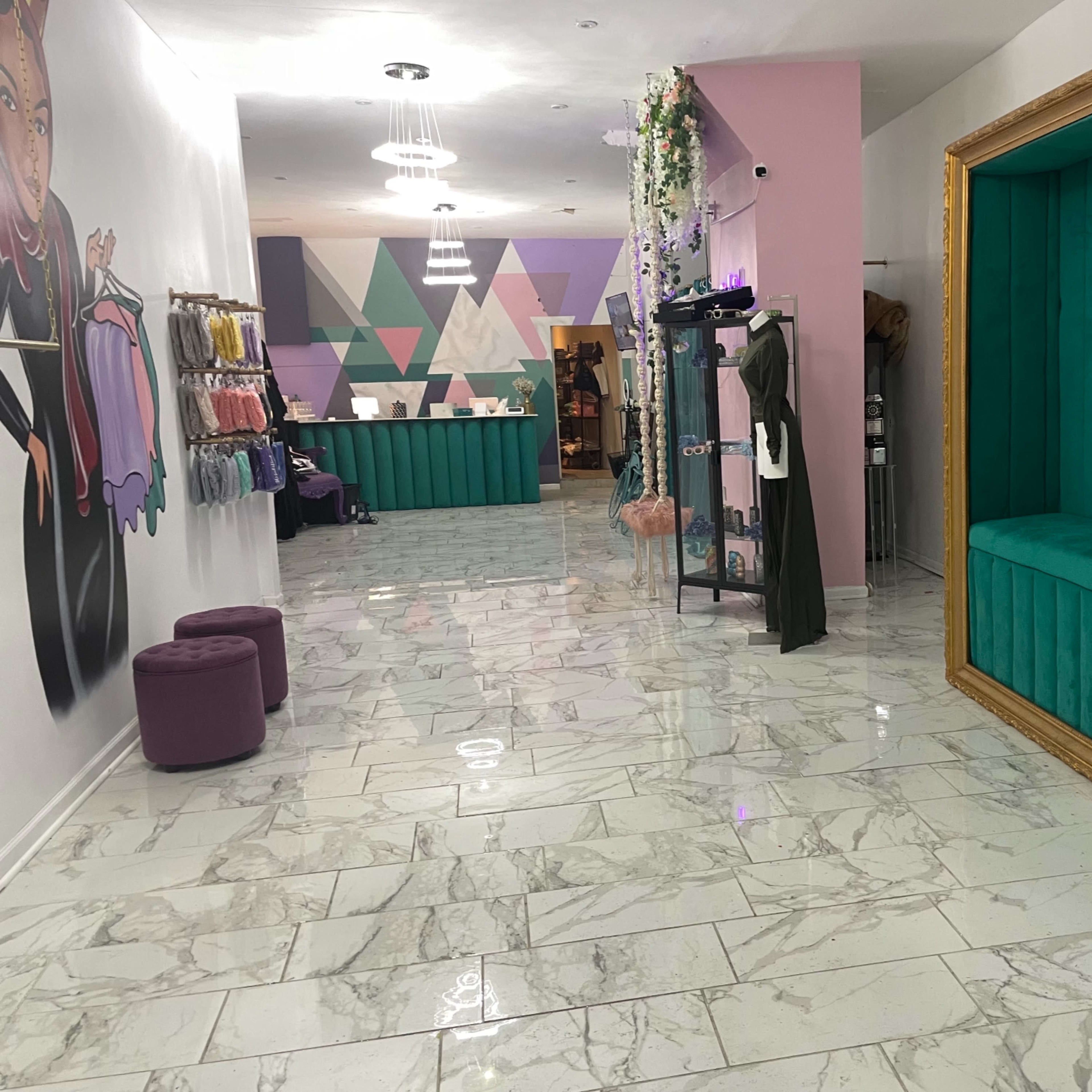 A brightly lit boutique interior with marble flooring, teal and pink walls, and a decorative seating area framed in gold.