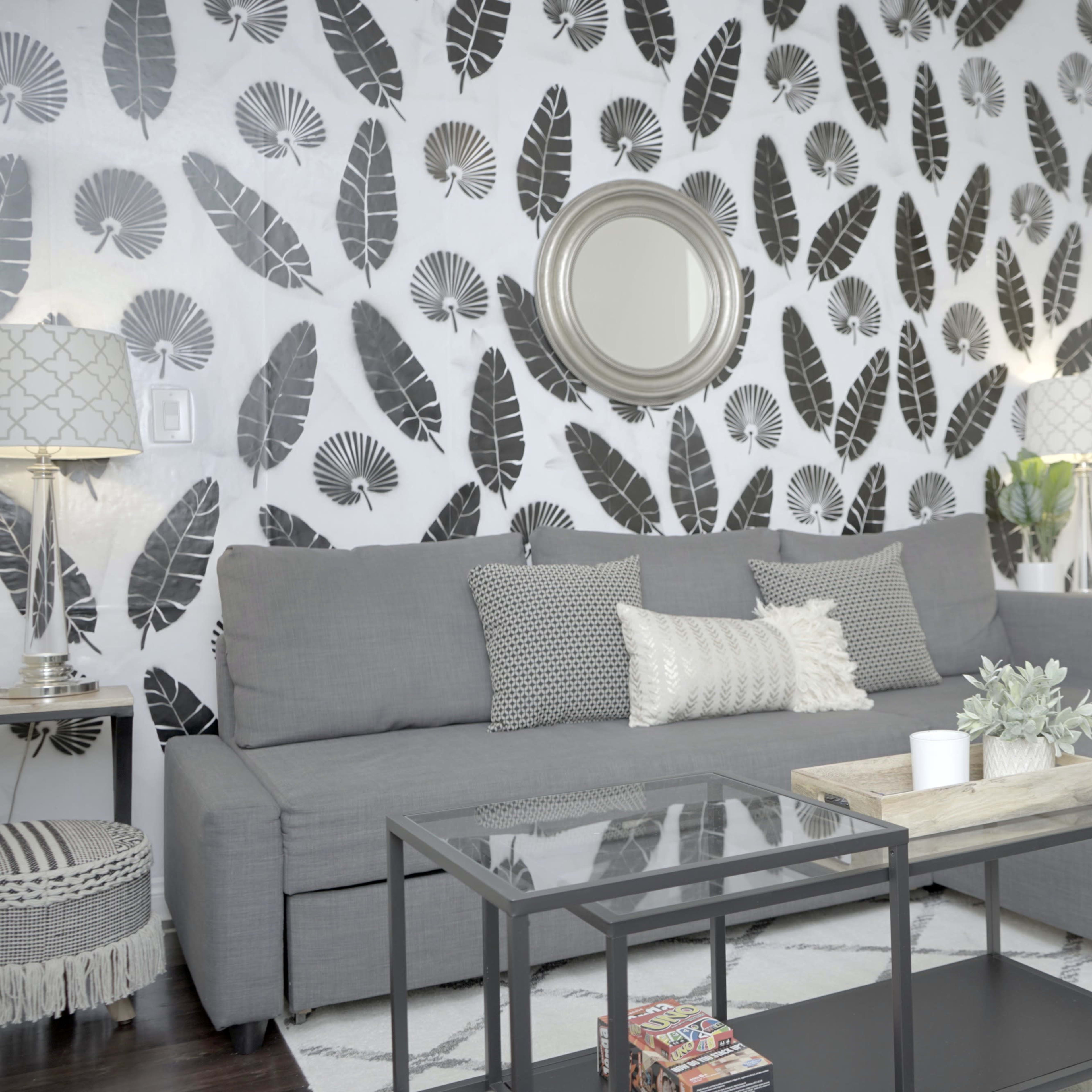 The living room features a gray sofa against a leaf-patterned accent wall, with a coffee table and decorative items in the center.
