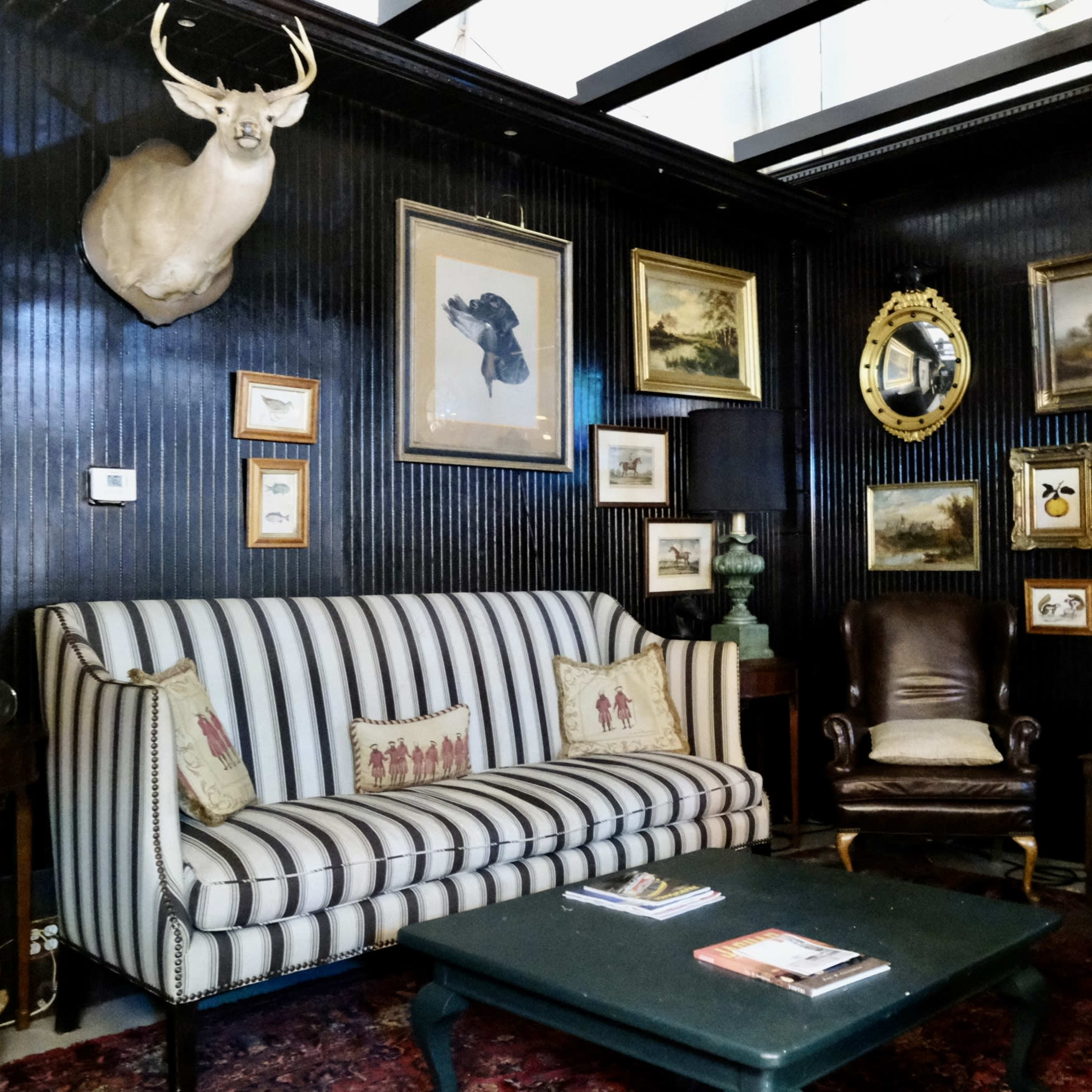 A cozy room featuring a striped sofa, leather armchairs, and a wall adorned with various framed artworks and decorative mirrors.