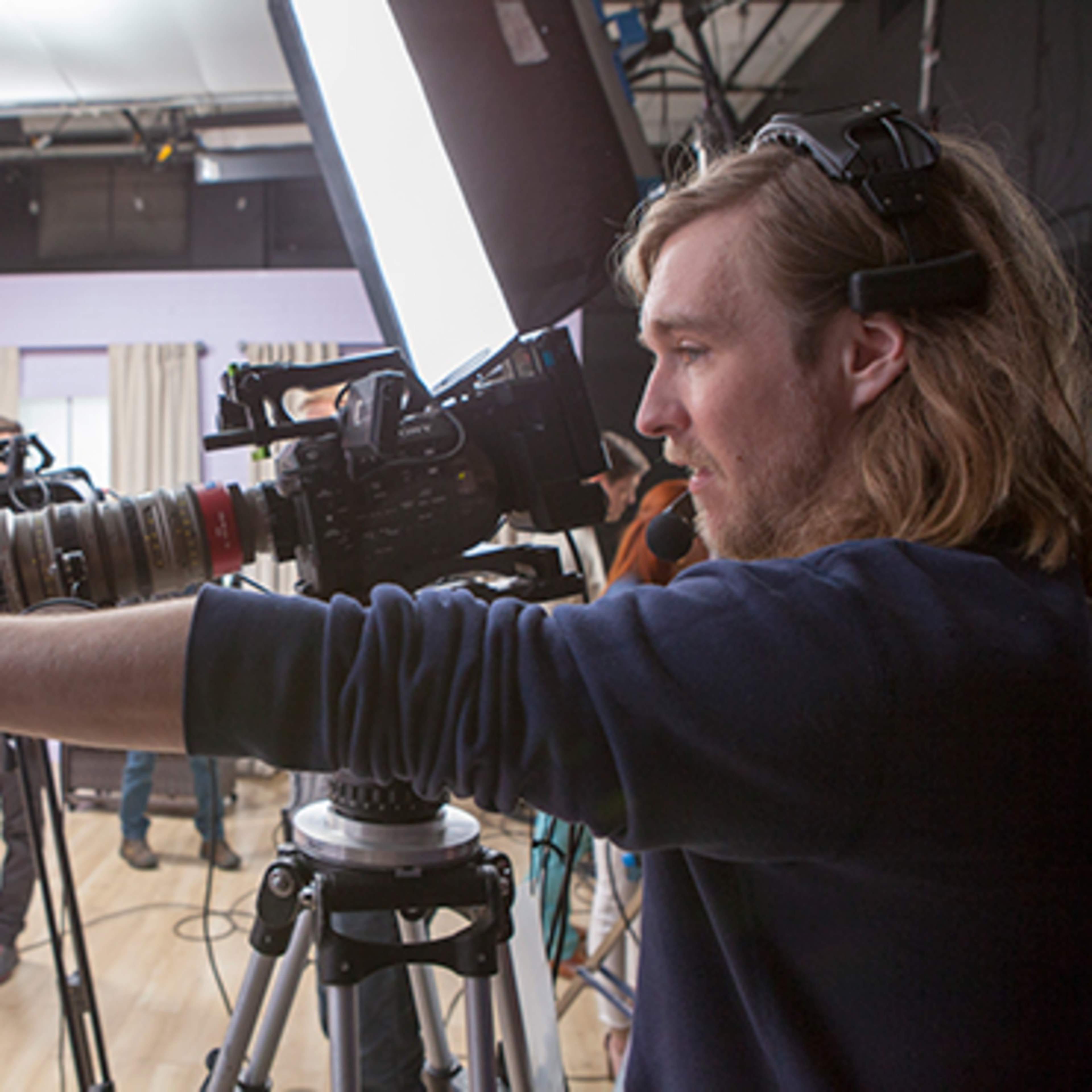 A crew member operates a camera on set, surrounded by other filming equipment and crew members.