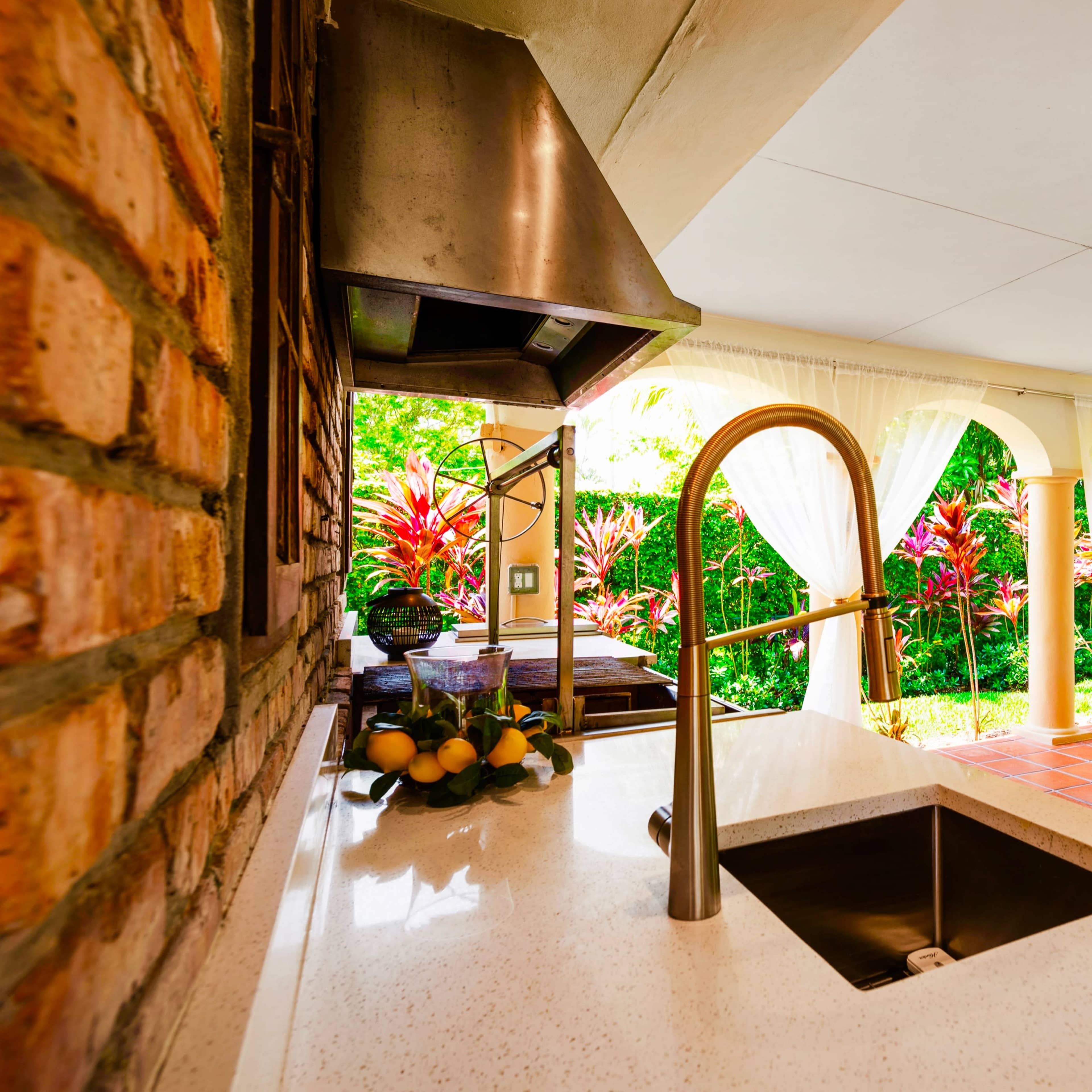 An outdoor kitchen area with a sink, a stone wall, and a dining space that opens to a lush garden.