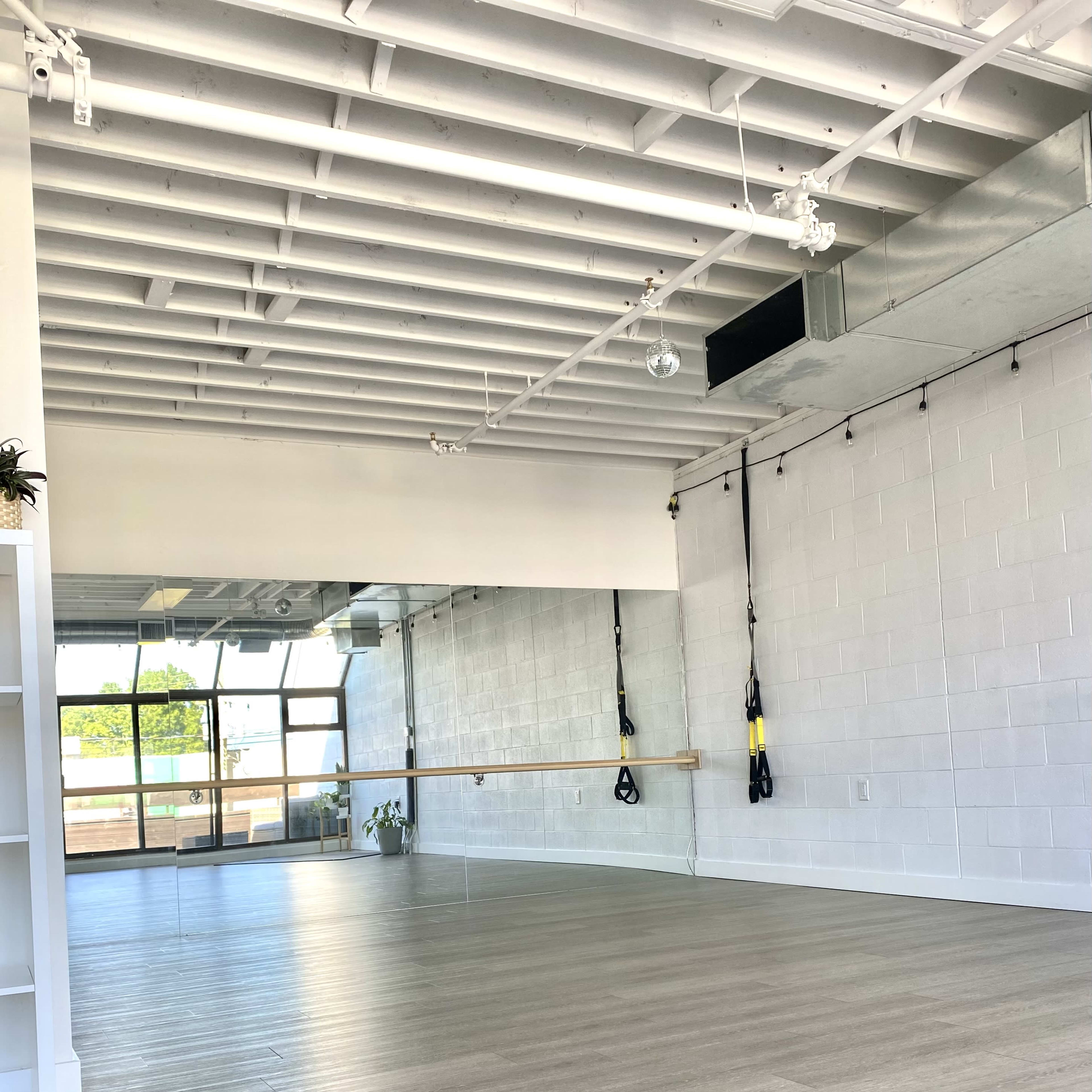 A spacious, well-lit exercise studio with wooden flooring and large mirrors on one wall.