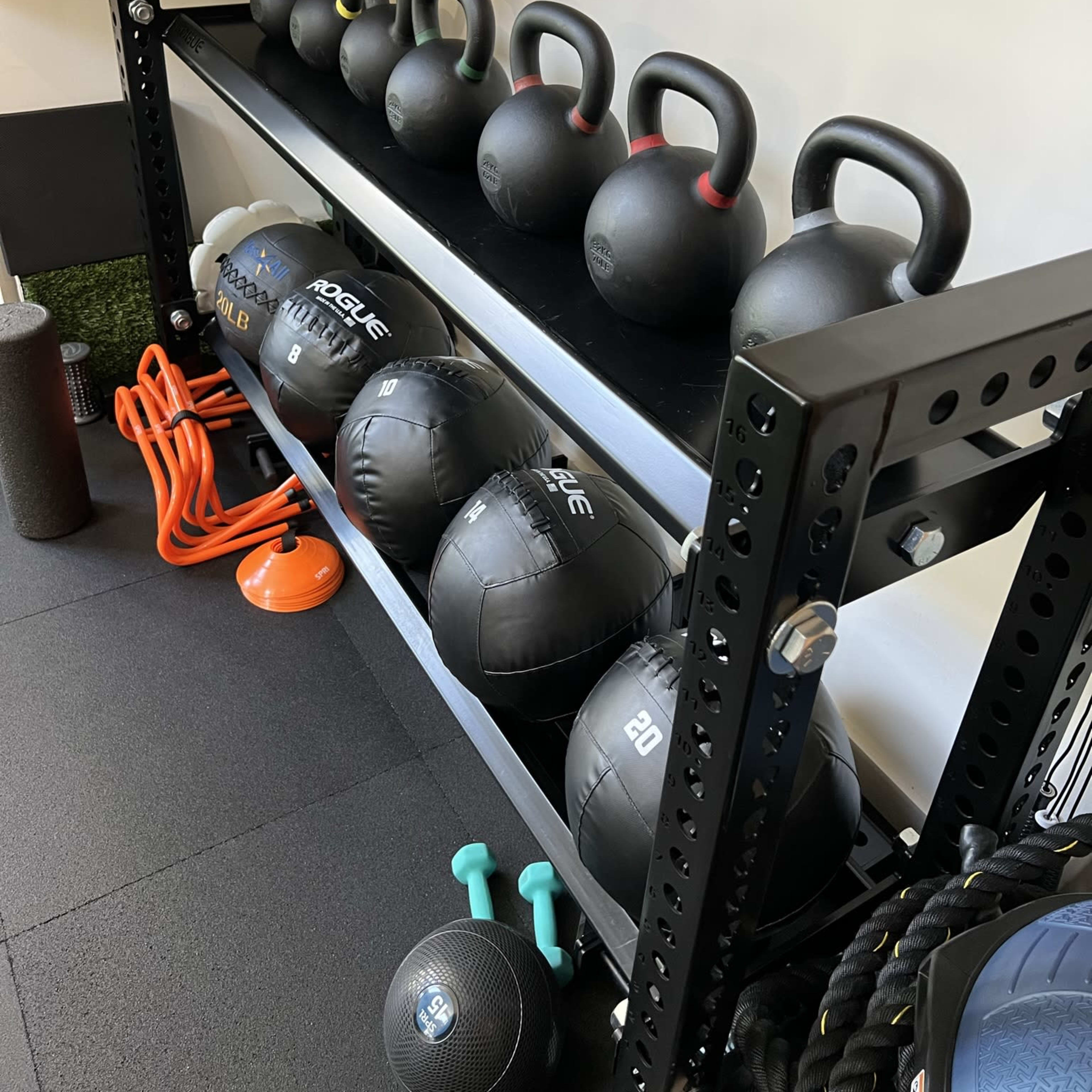 A fitness equipment storage rack organized with kettlebells and medicine balls in a workout space.