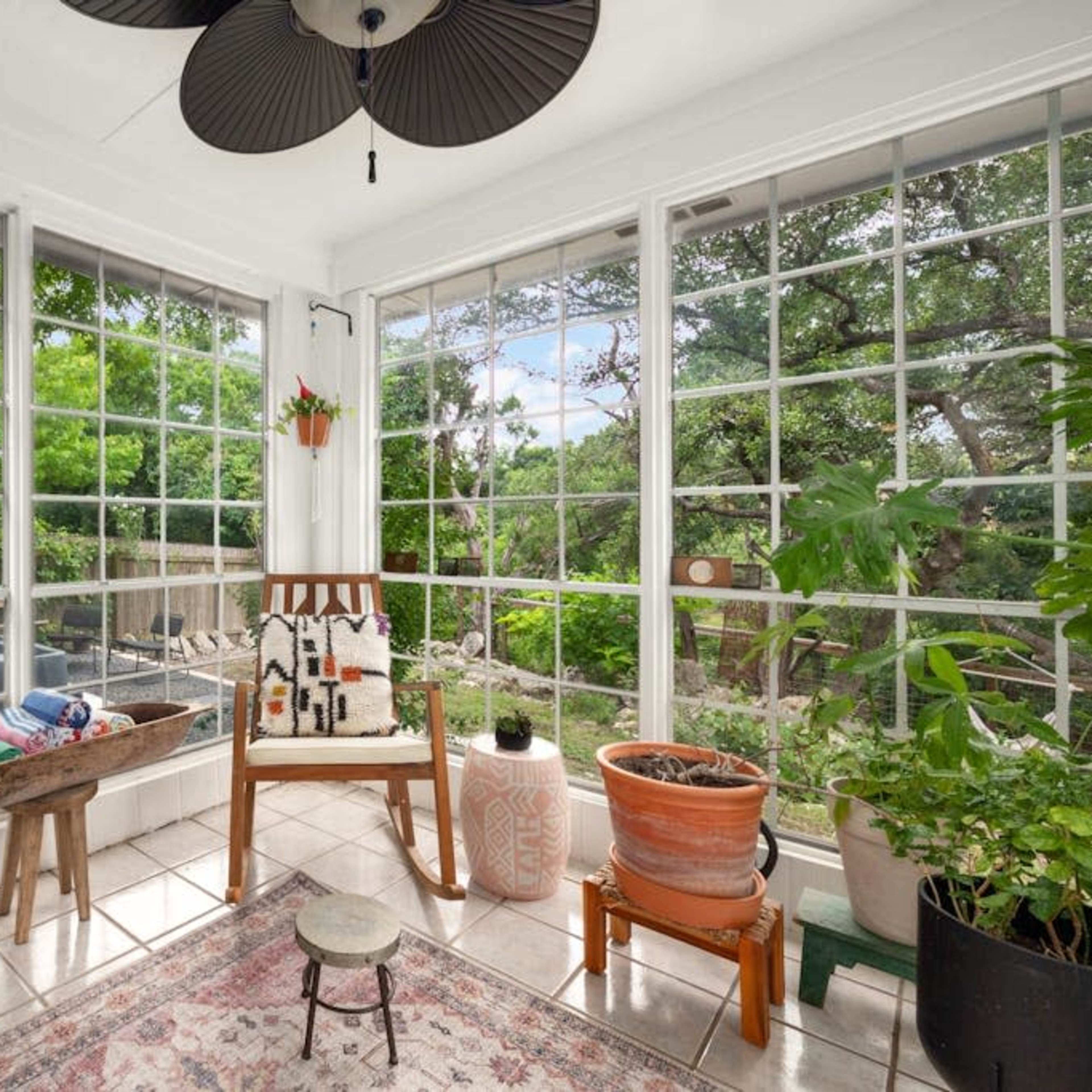 A sunlit sunroom with large windows, a chair, potted plants, and a small table.