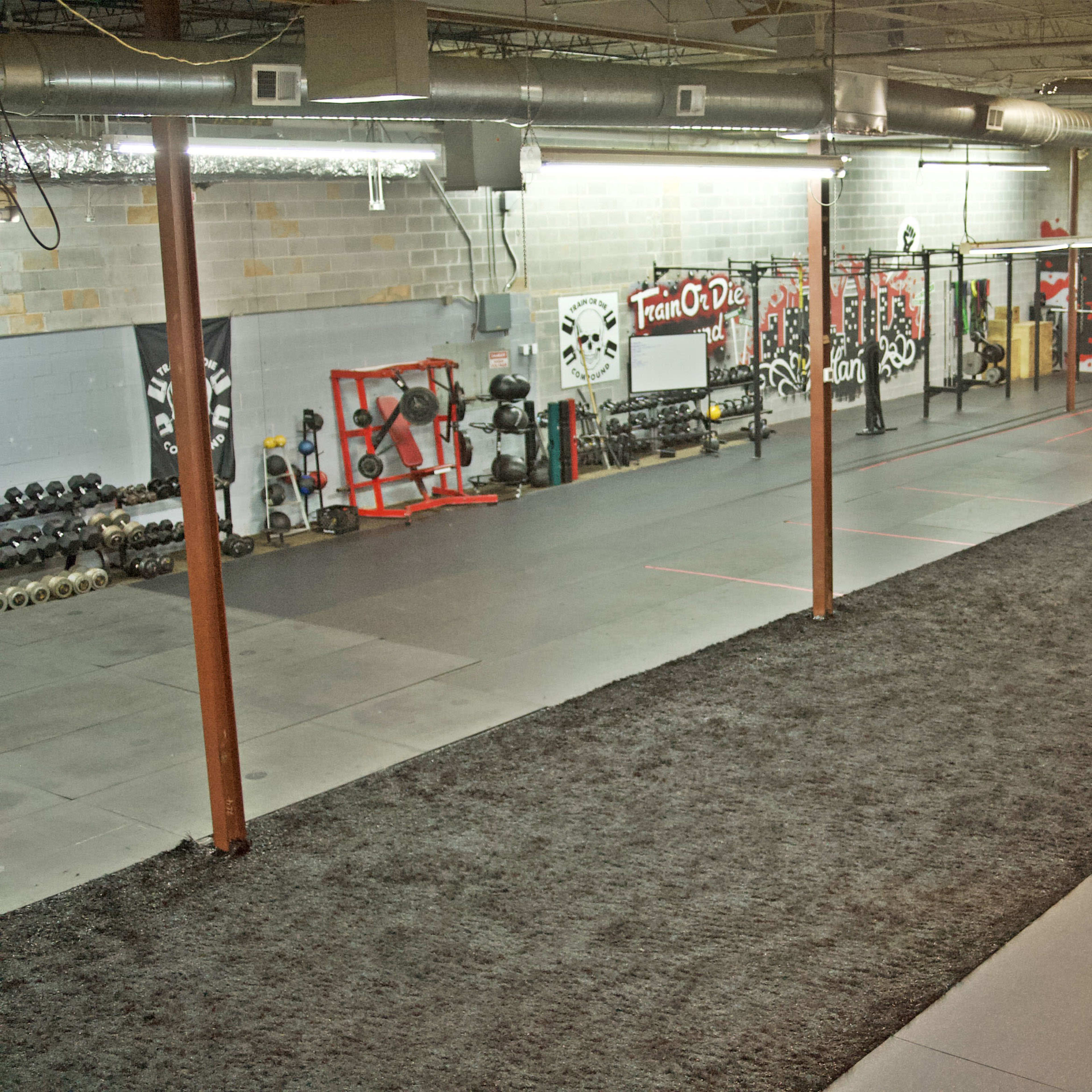 A spacious gym interior with exercise equipment, including free weights and a long turf area for workouts.