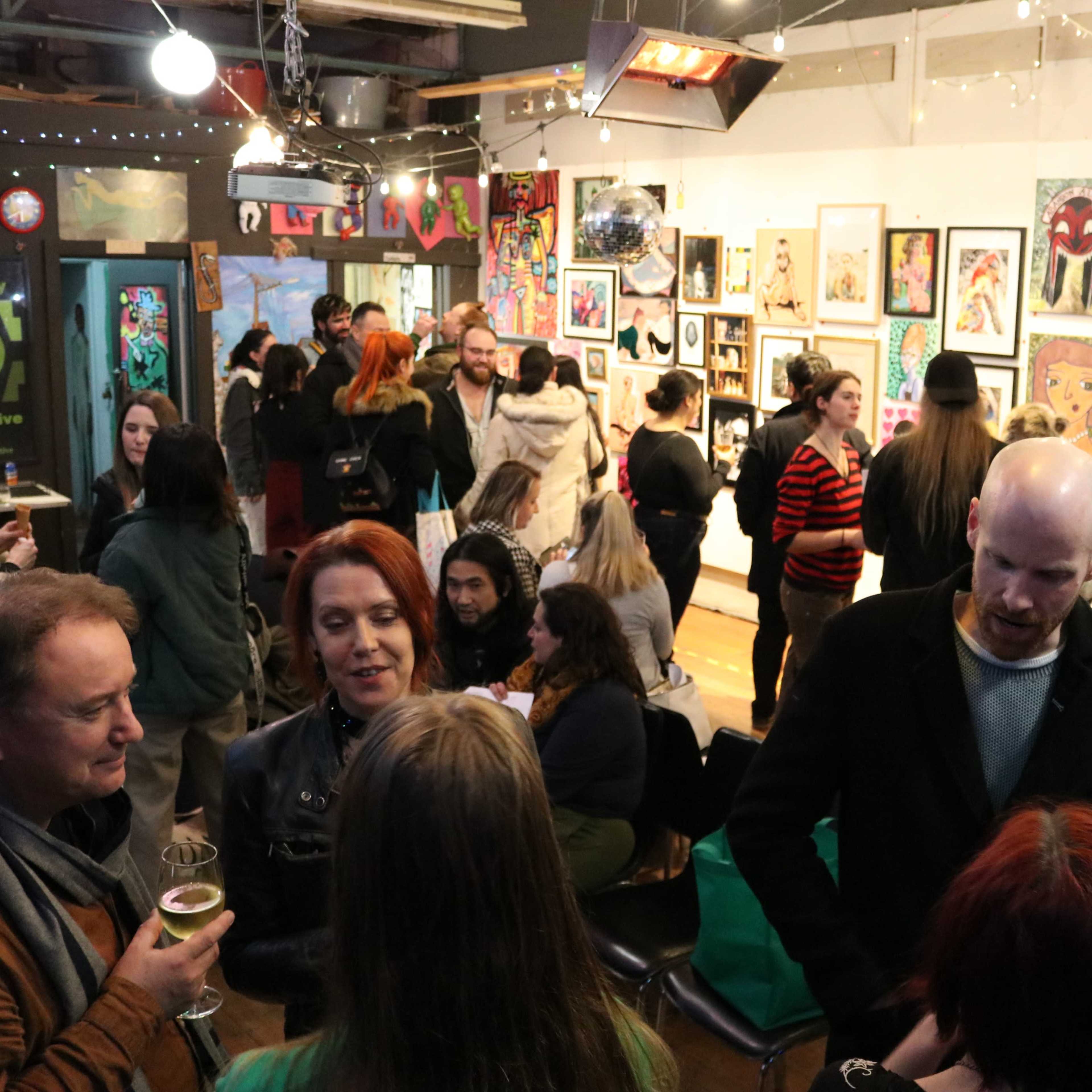 A group of people mingles in an art gallery filled with colorful artworks and various decorative lights.