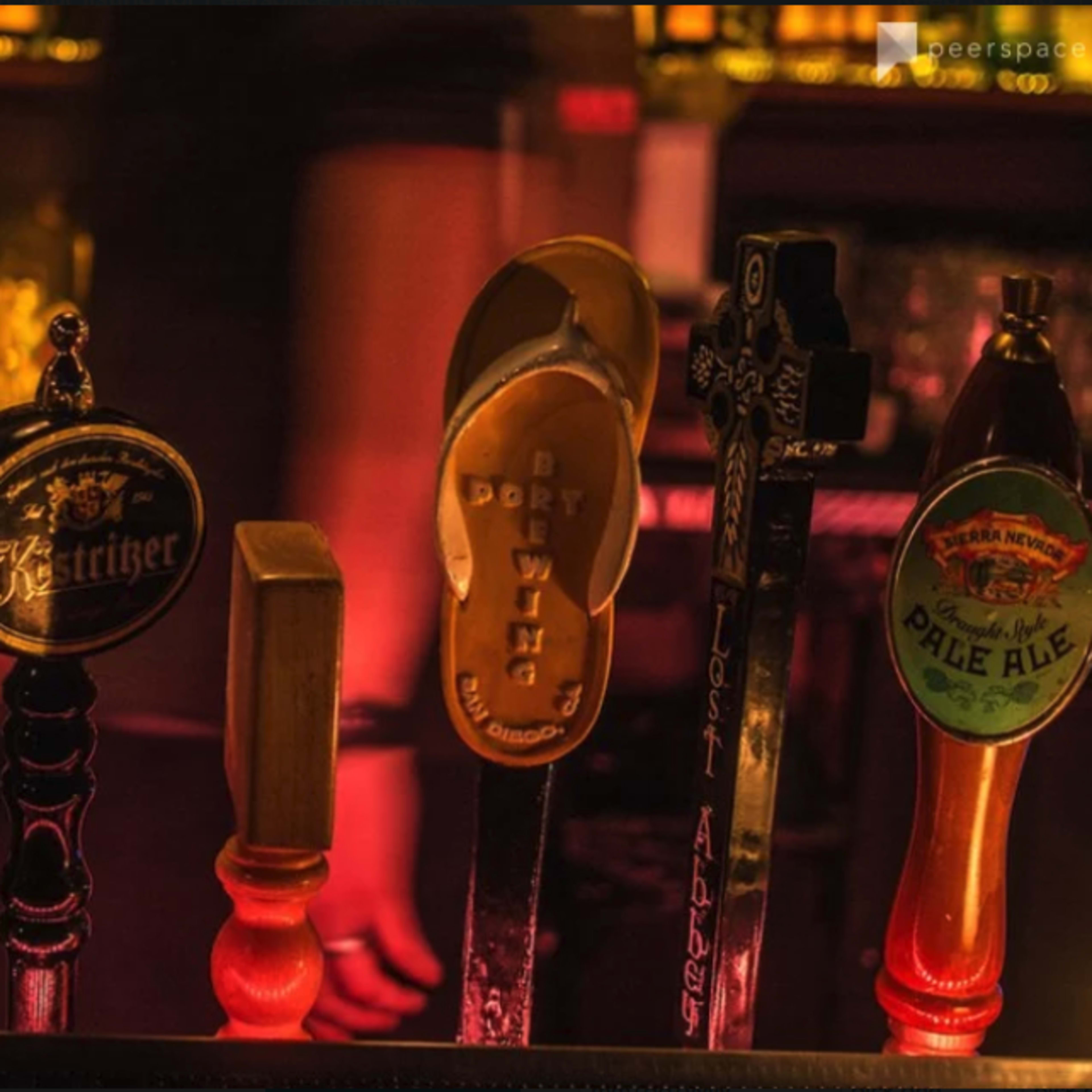 A lineup of beer taps with various labels and a single flip-flop on one of the handles.