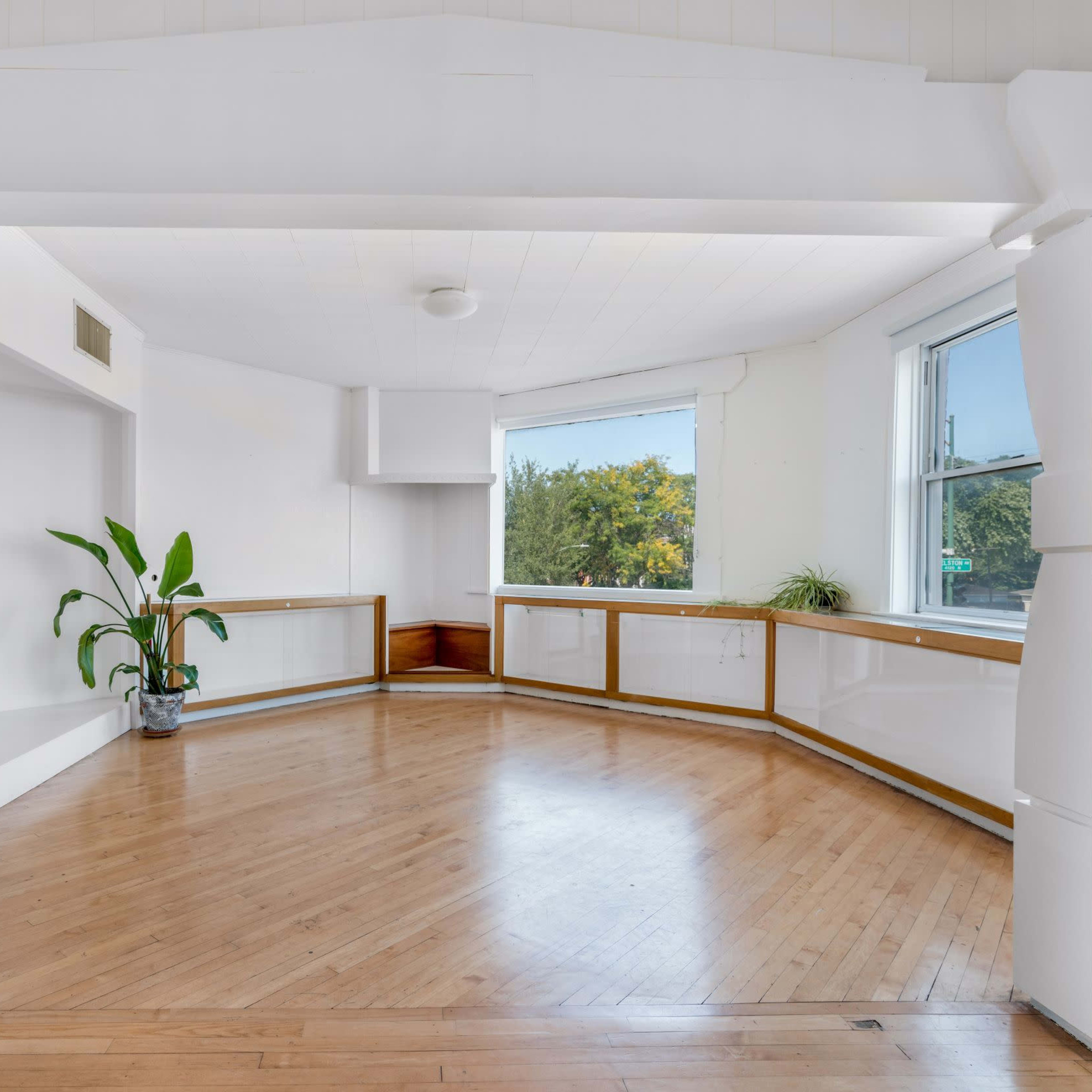 A spacious room features large windows, hardwood flooring, and a curved wall with built-in shelving.