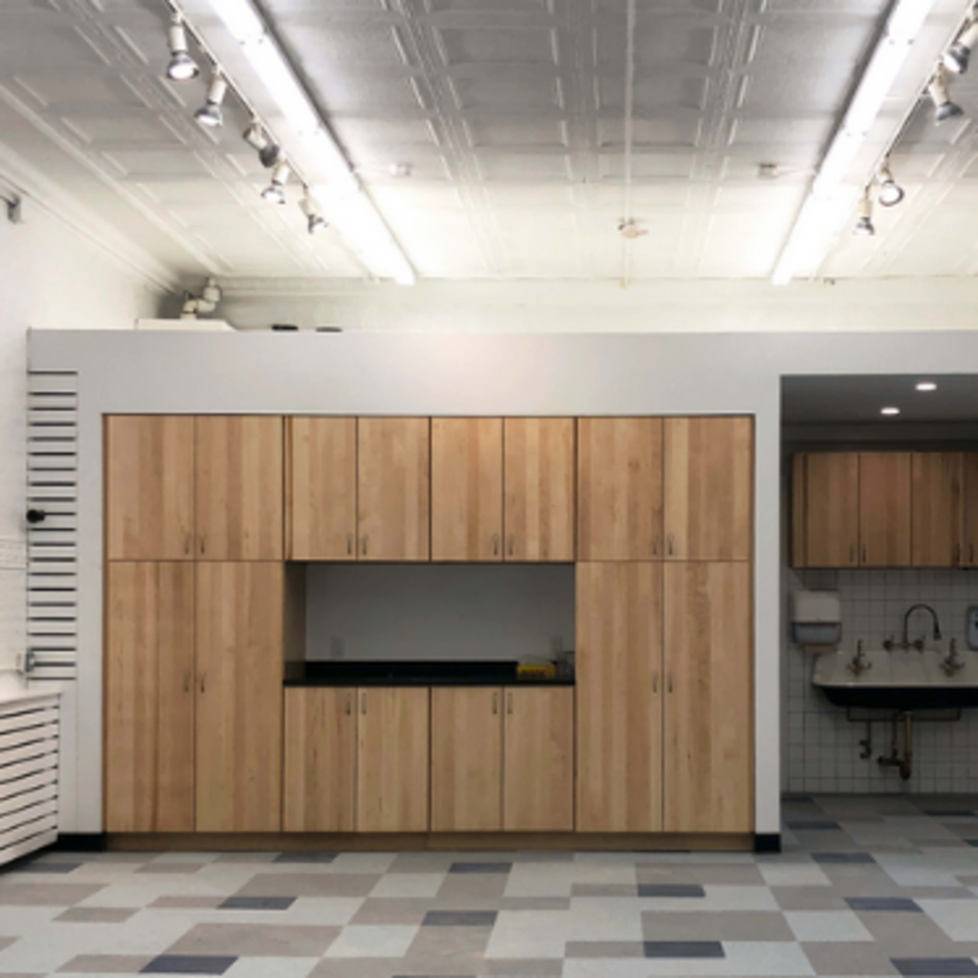 A spacious room with wooden cabinetry and a sink area, featuring a tiled backsplash and a patterned floor.