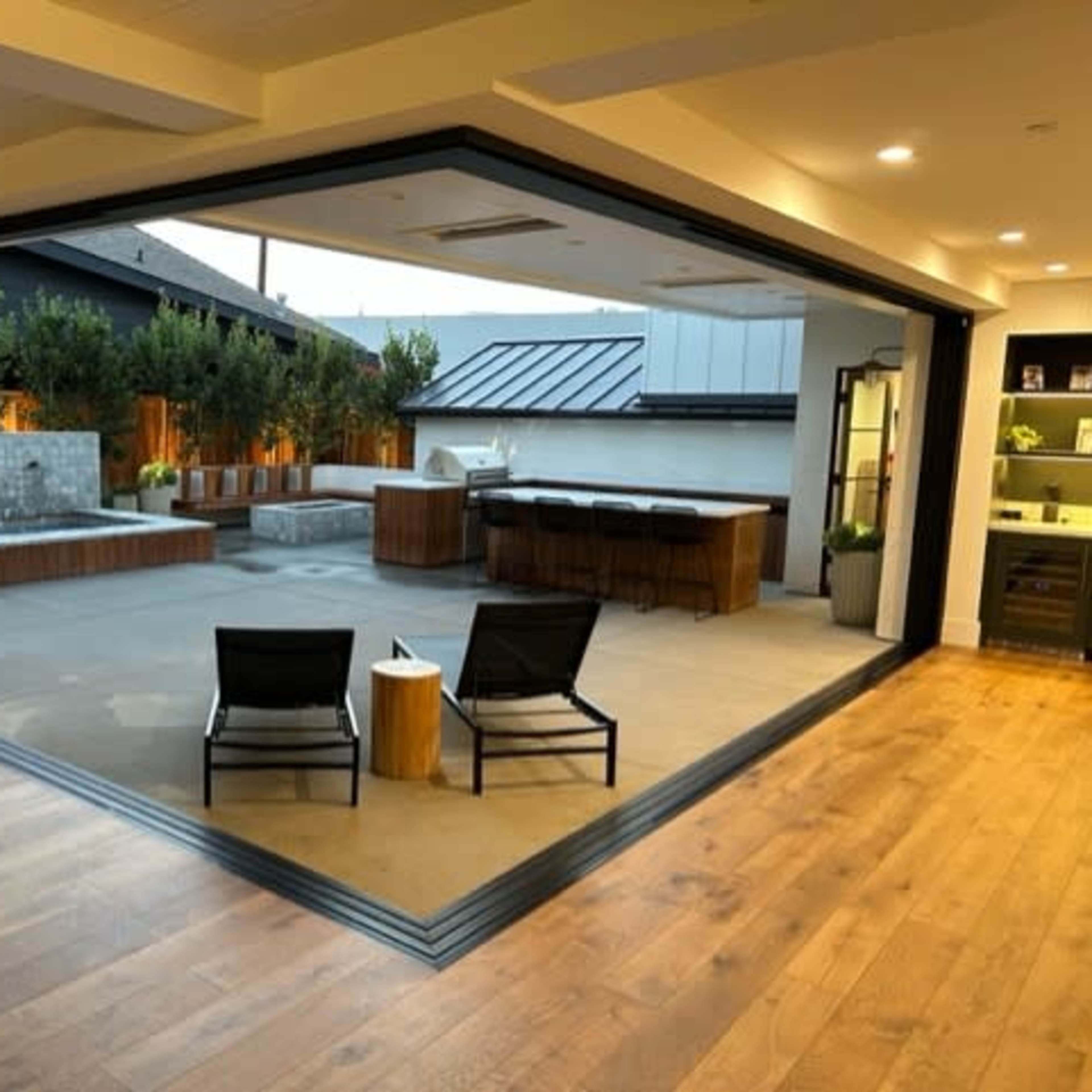 An open modern living space leading to an outdoor area with a jacuzzi, seating, and a kitchen.