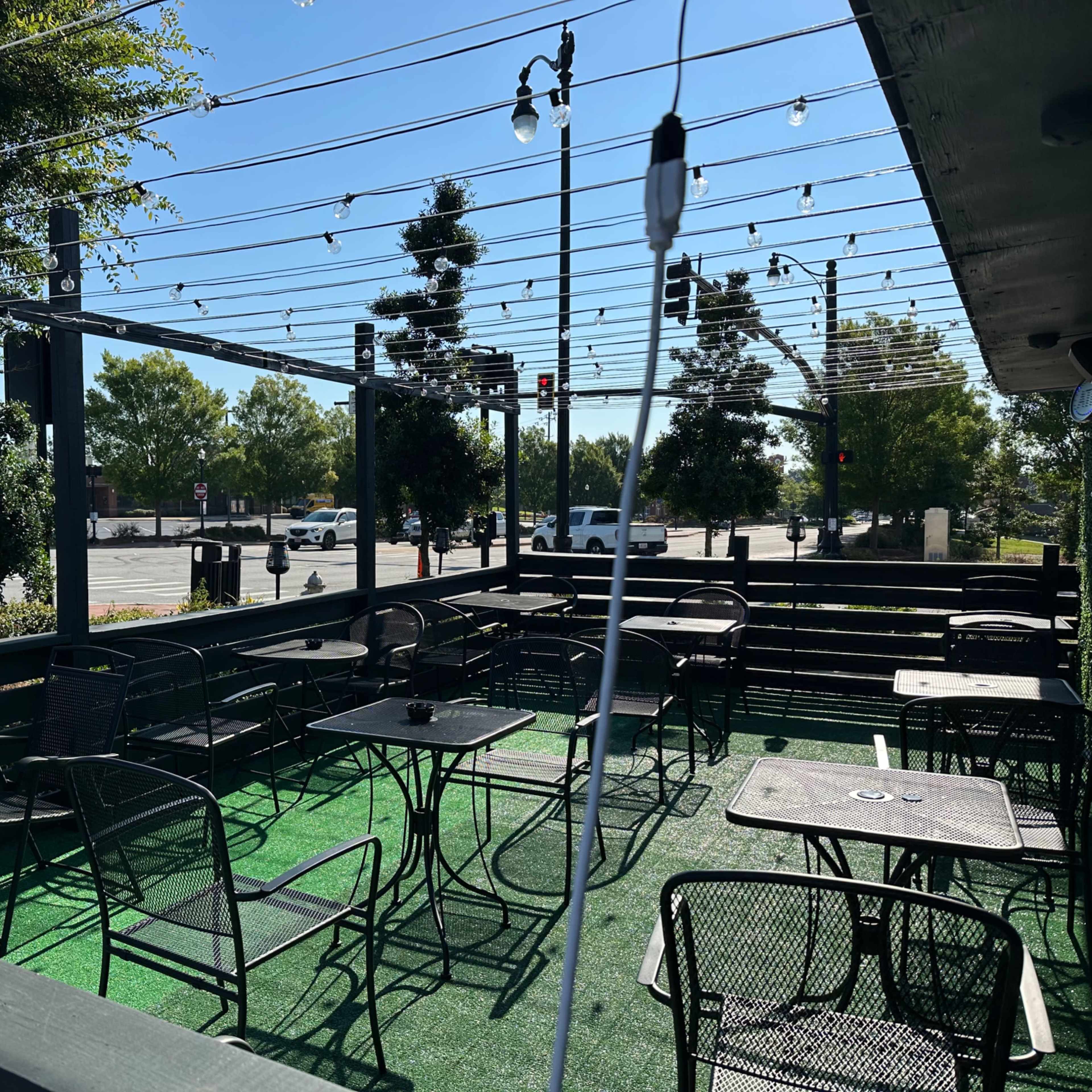 An outdoor dining area with empty tables and chairs arranged on a green carpet under string lights.