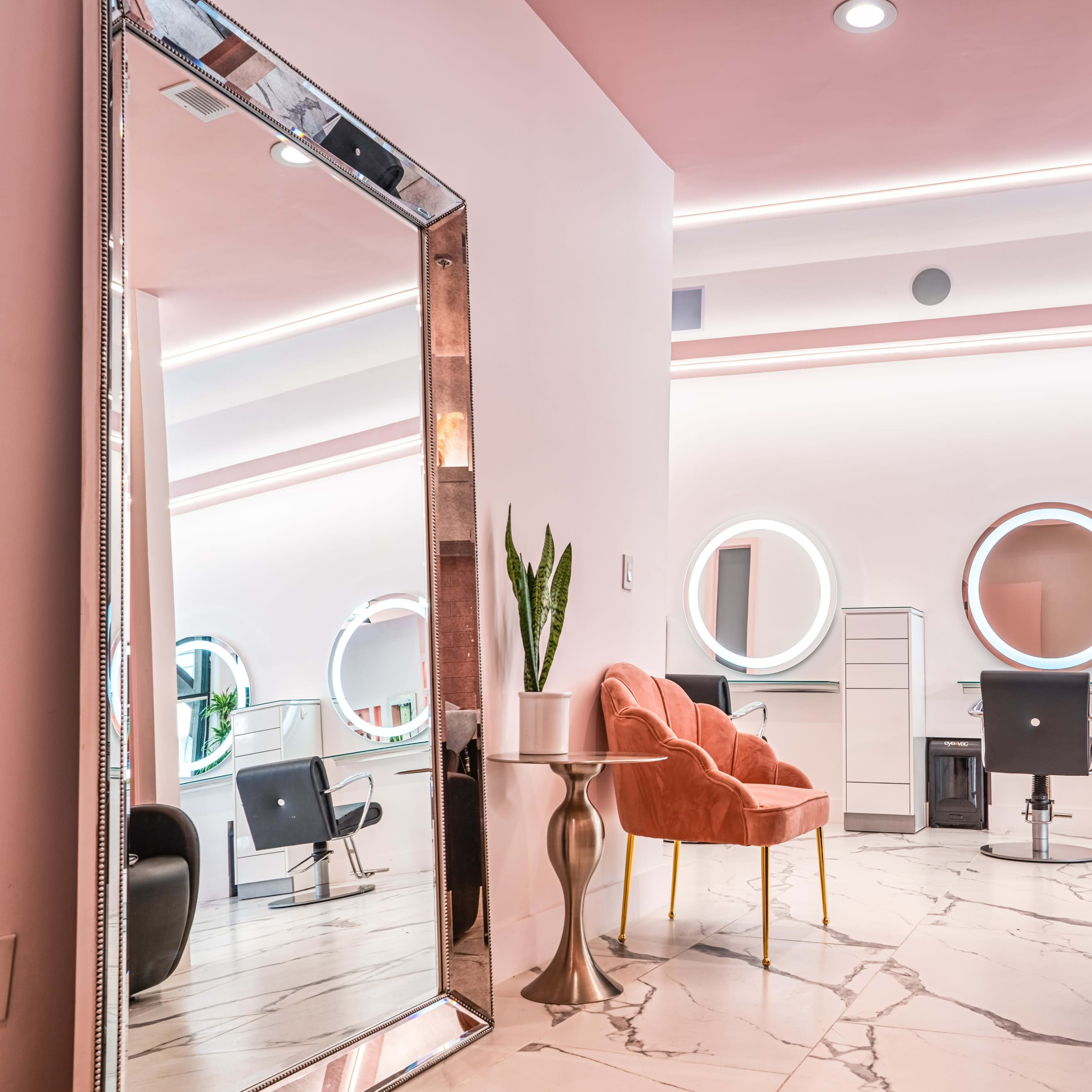 A modern hair salon interior featuring a large mirror, circular mirrors on the walls, a stylish chair, and a marble floor.