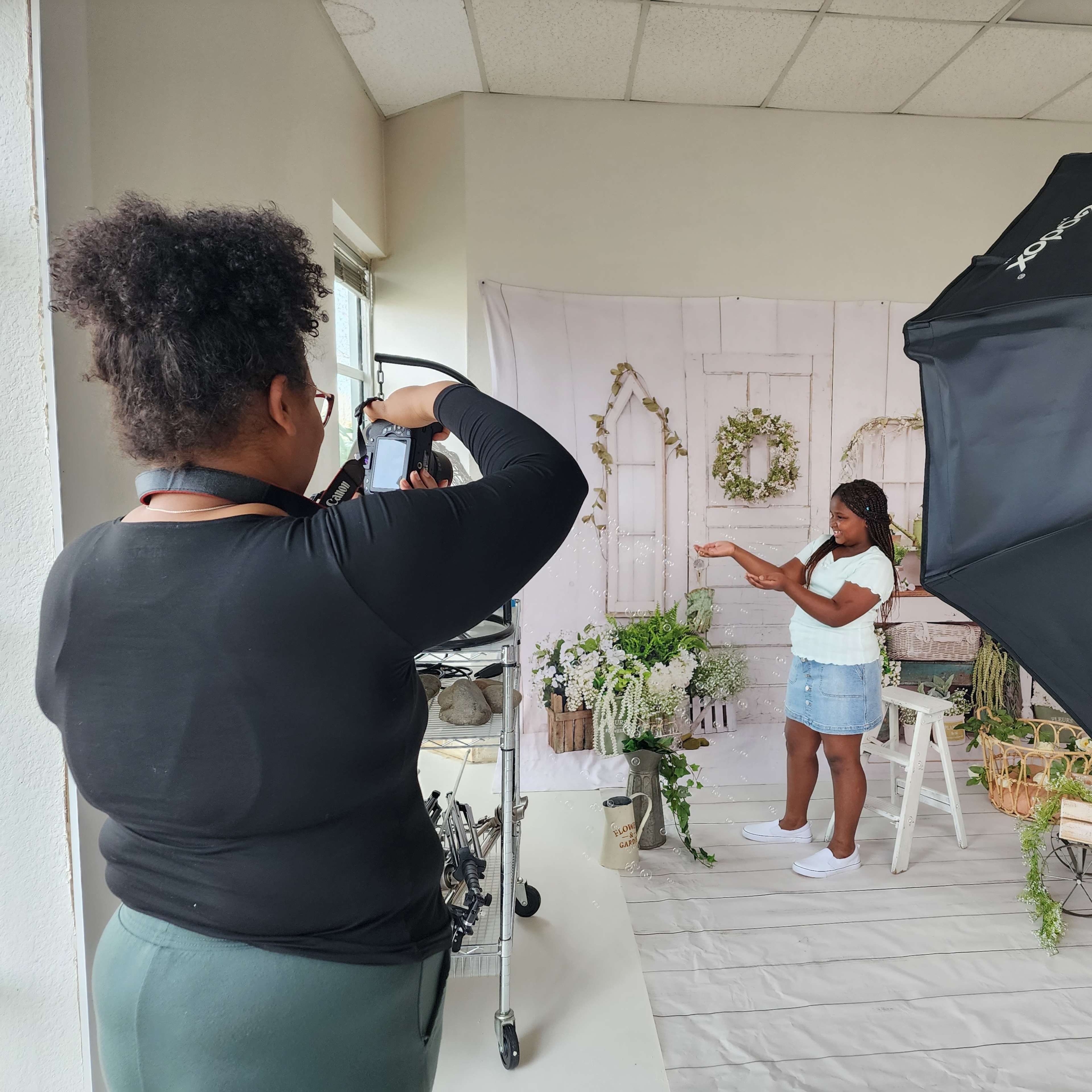 A photographer captures a model posing with greenery in a studio setting adorned with a backdrop and lighting equipment.