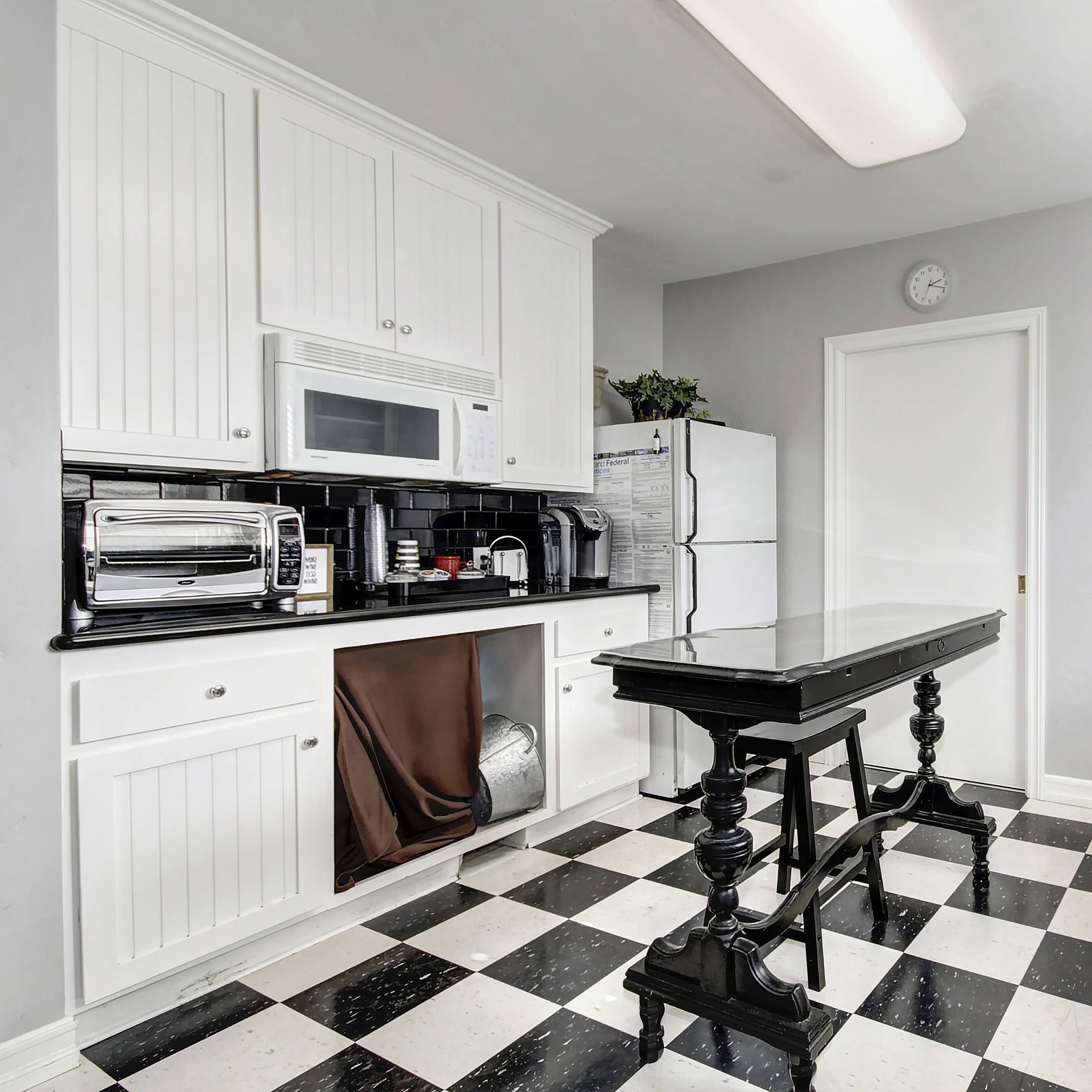 The kitchen features black and white checkered flooring, white cabinetry, and modern appliances arranged around a central black table.